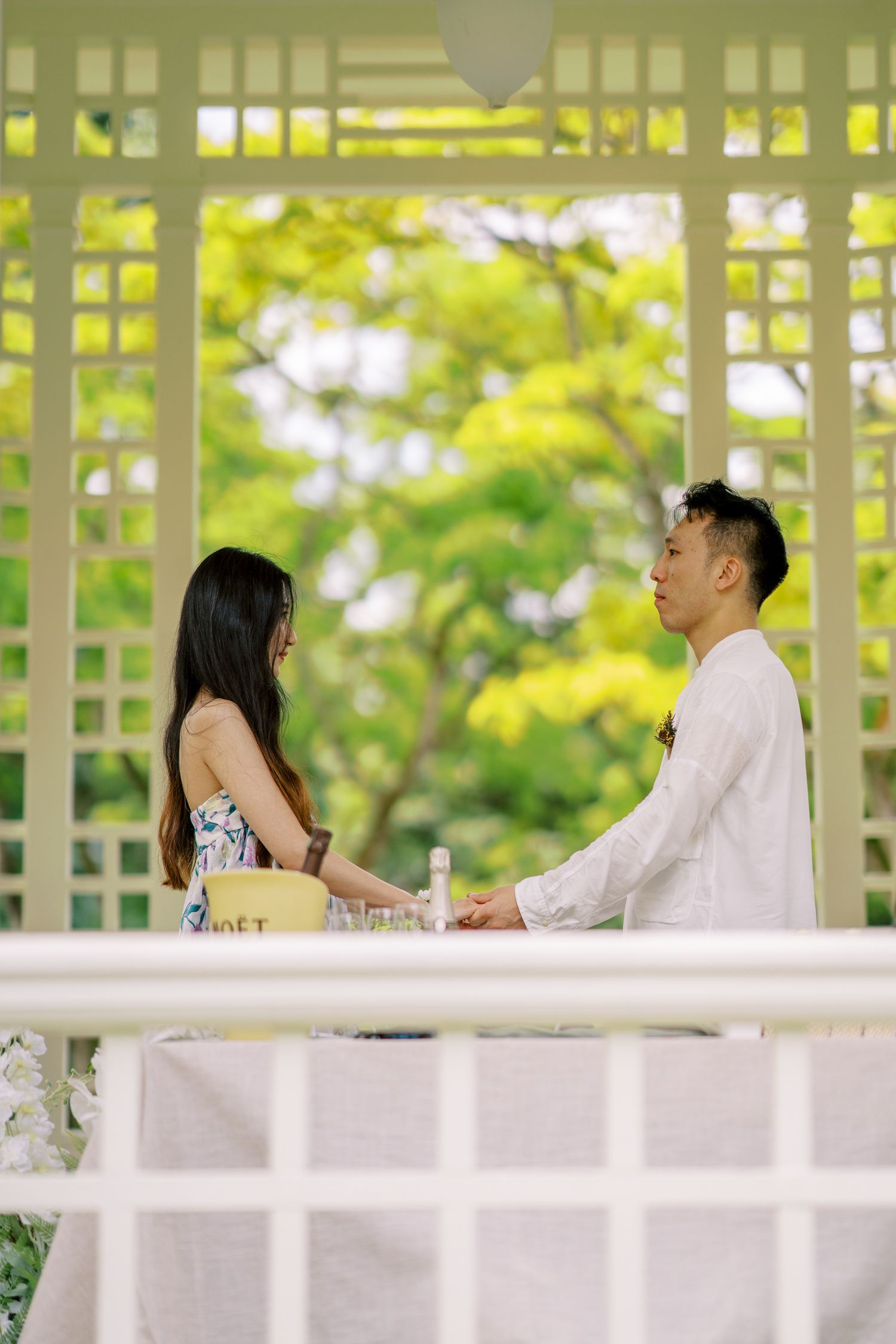 People gather in a bright outdoor pavilion with latticed walls and natural lighting.