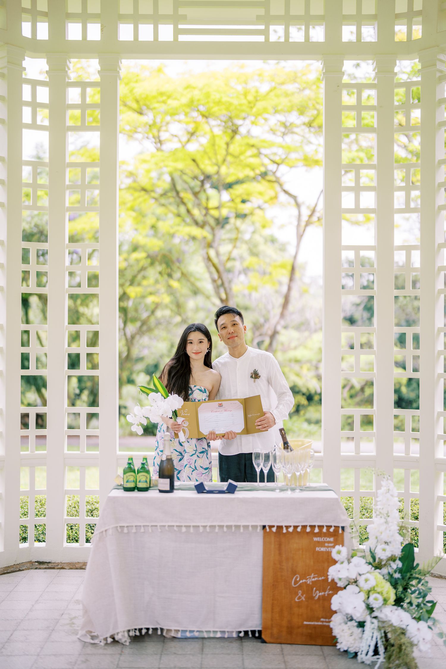 Elegant outdoor celebration setup with champagne and flowers in a white latticed pavilion.