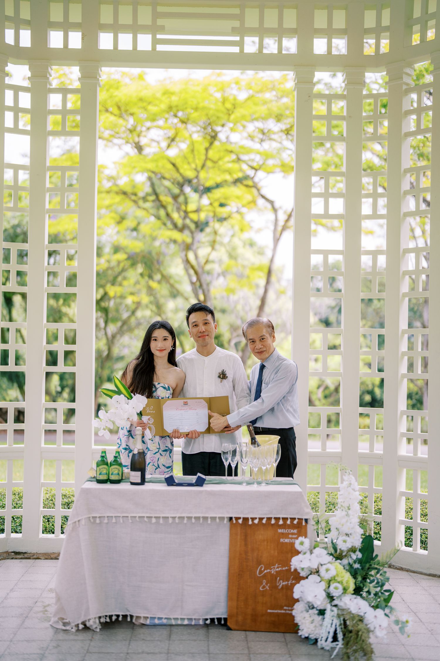 Couple celebrating with champagne in an elegant white gazebo surrounded by lush greenery.