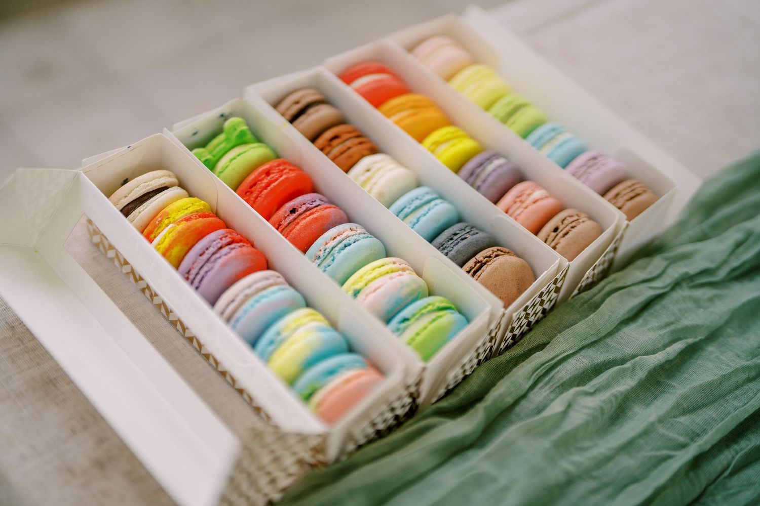 Colorful macarons arranged in neat rows in a display box with green fabric accent.