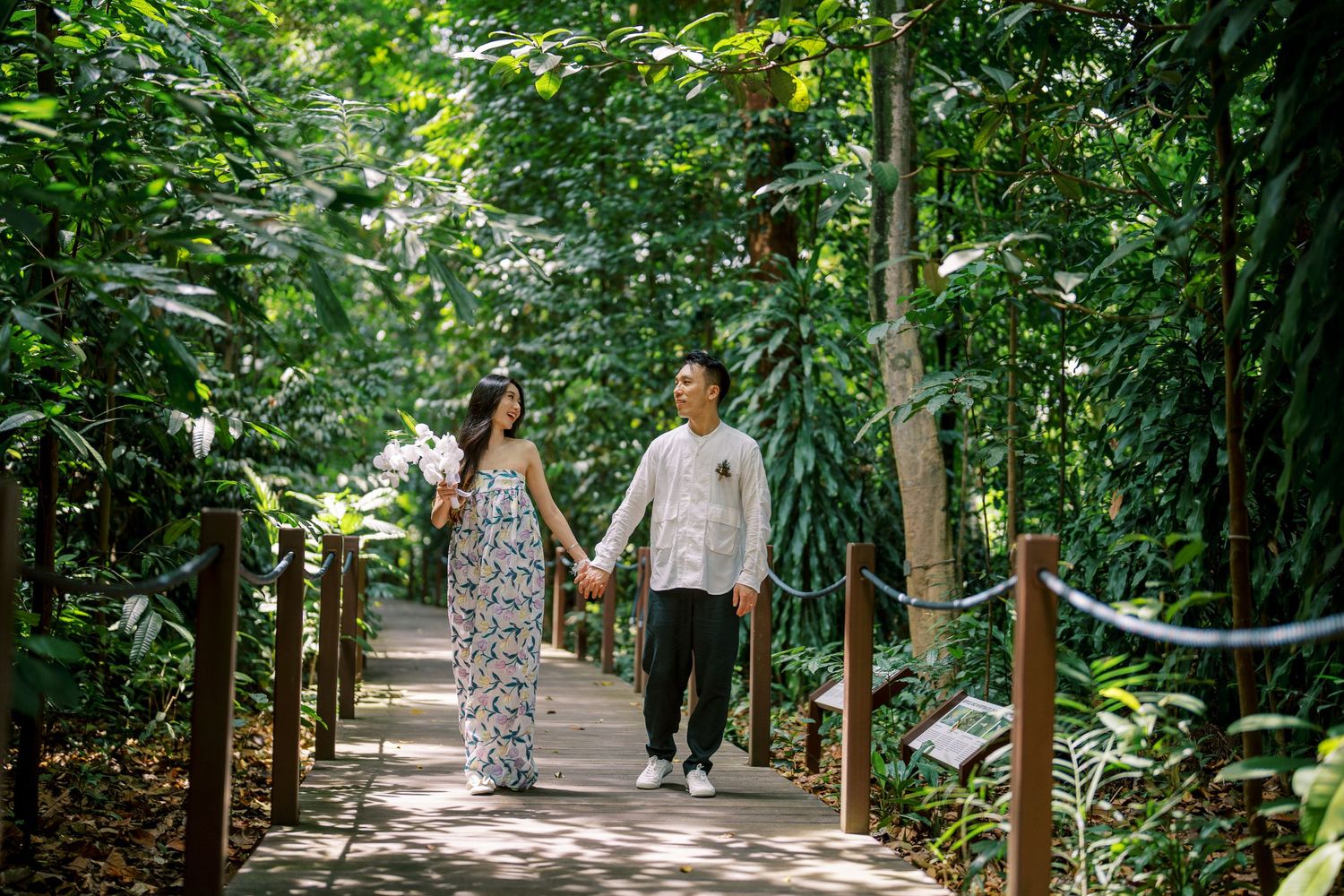 Two people walk together on a winding garden path surrounded by lush tropical plants.