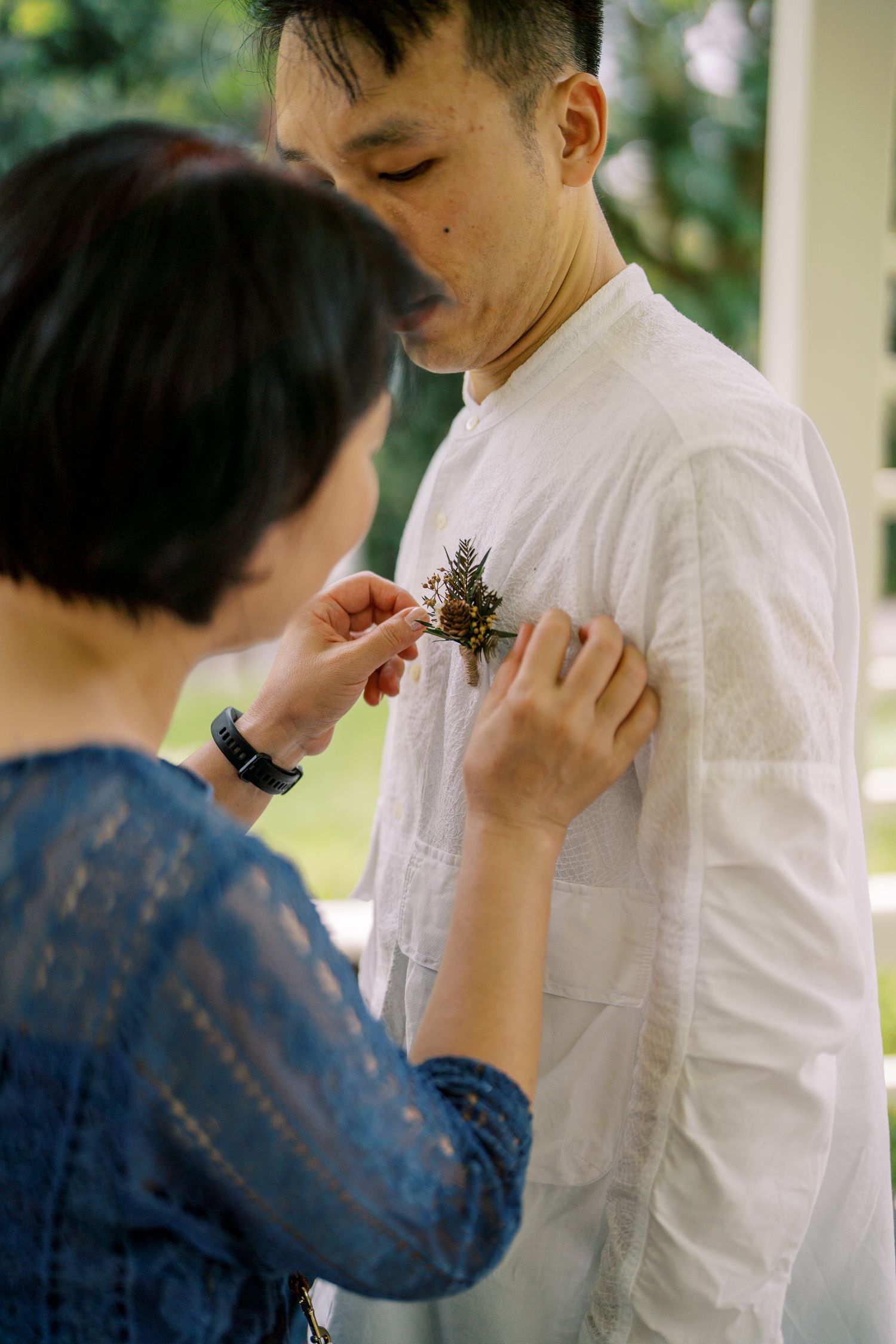 Close-up of boutonniere being pinned on white shirt in outdoor setting.