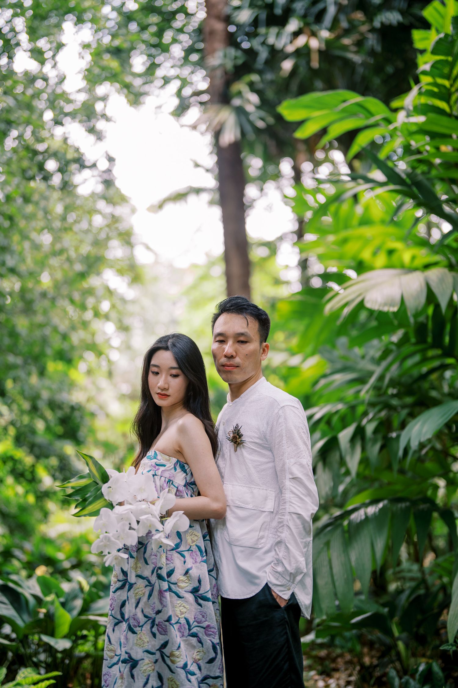 Couple embraces in a romantic garden photoshoot surrounded by tropical greenery.