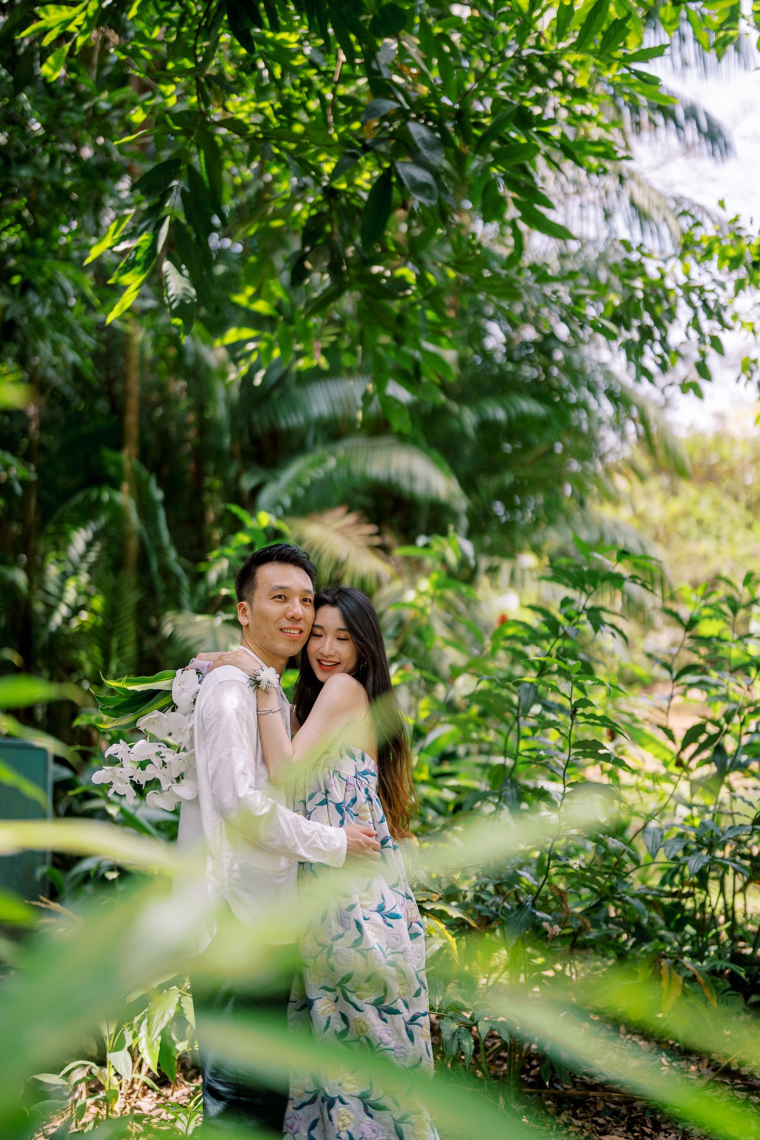 A romantic couple shares an intimate moment among lush tropical greenery in matching floral outfits.
