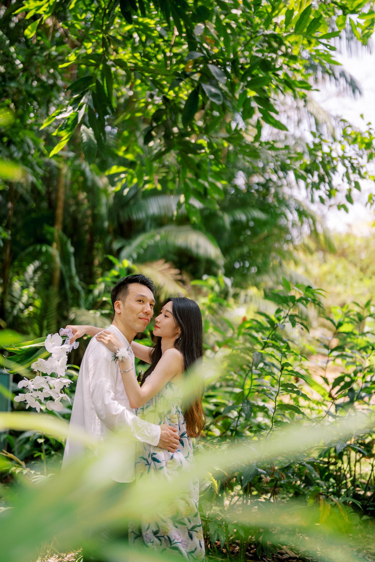 A couple embraces in a garden setting with green foliage framing the romantic scene.