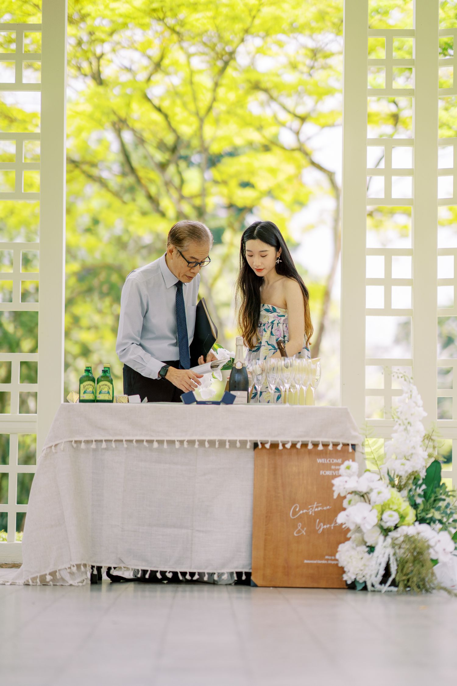 Wedding reception setup with drinks station in white gazebo decorated with flowers.
