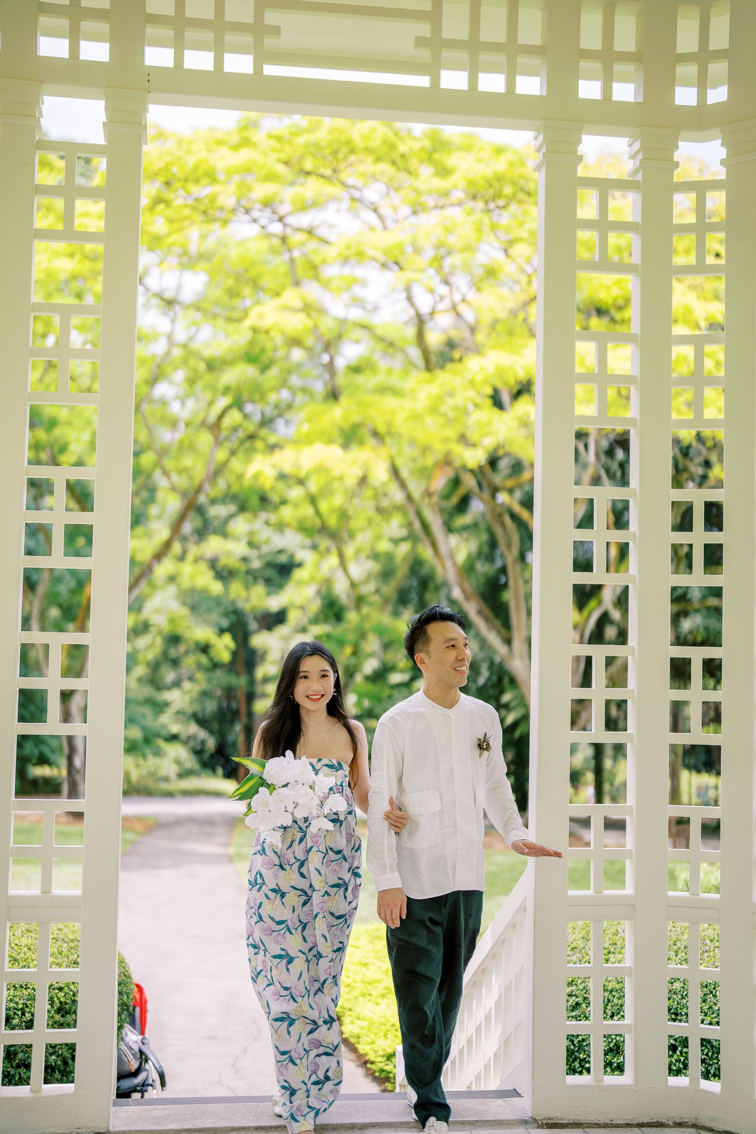 A peaceful garden scene with people walking through a white architectural pergola structure.