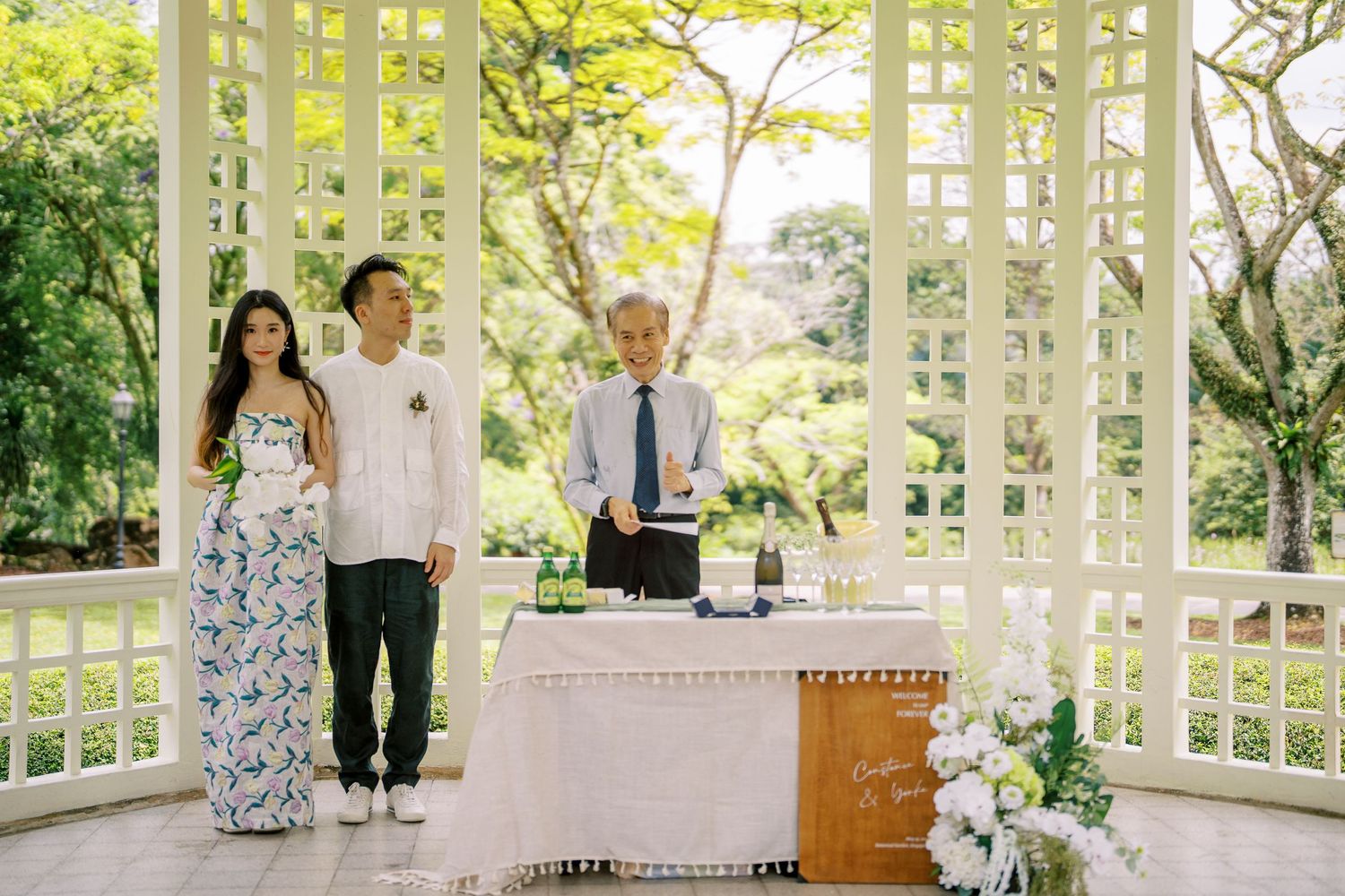An intimate gathering takes place under a white latticed pavilion with decorative floral arrangements.