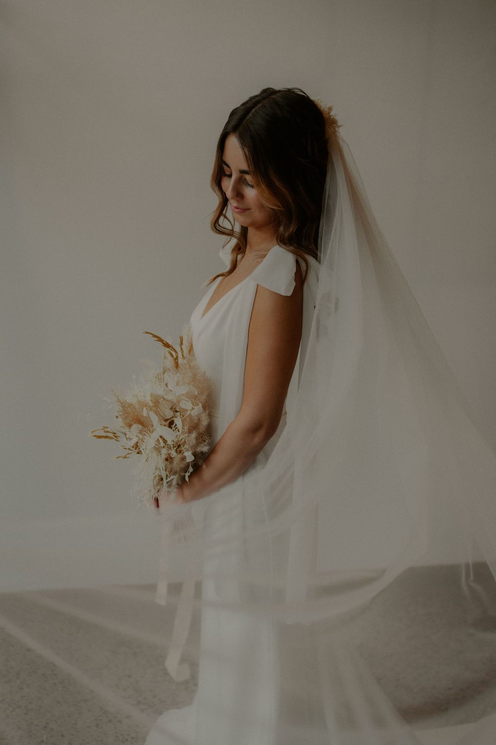 Classic white wedding dress with sheer veil and dried flower bouquet in natural light.