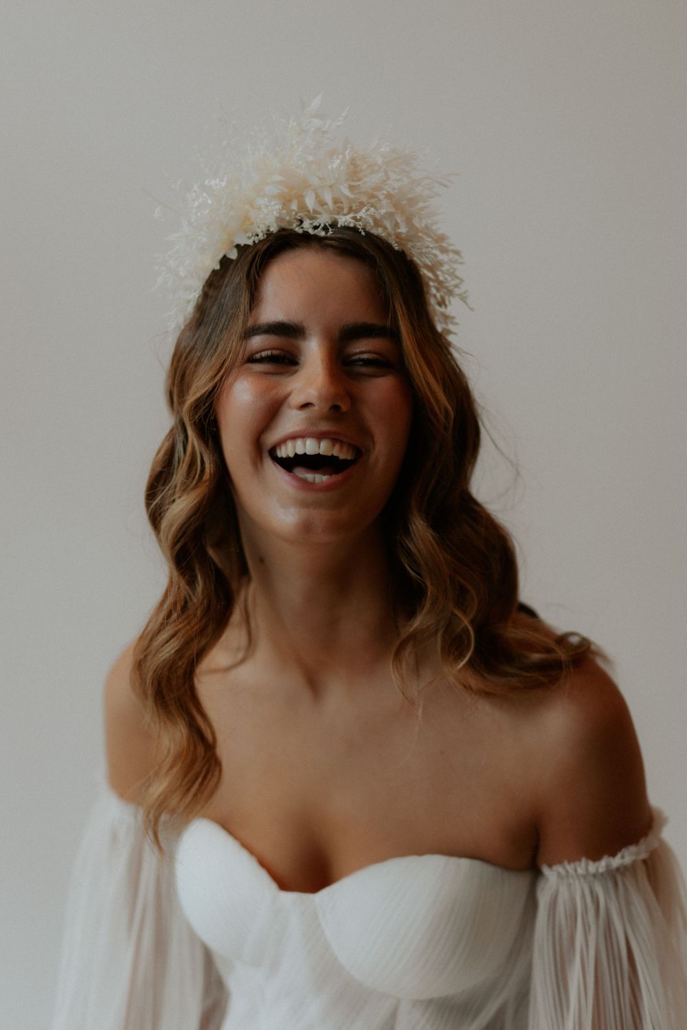 Joyful bridal portrait with delicate crown and off-shoulder wedding dress.