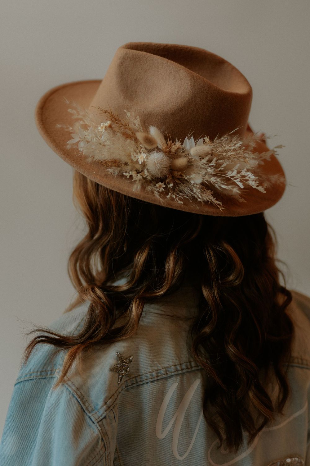 A brown felt hat decorated with dried flowers photographed from behind.