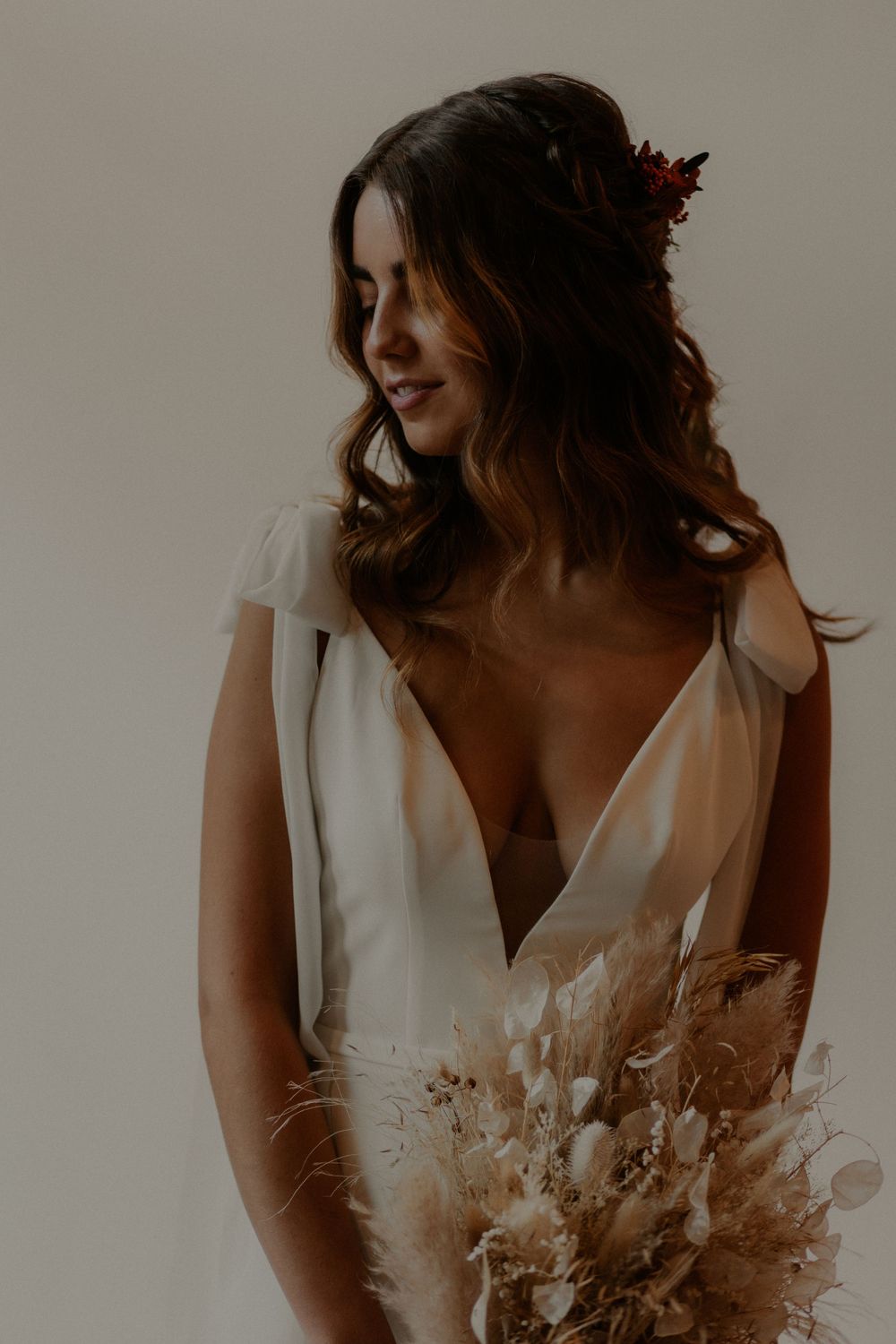 Delicate white bridal gown with plunging neckline and dried flower bouquet.