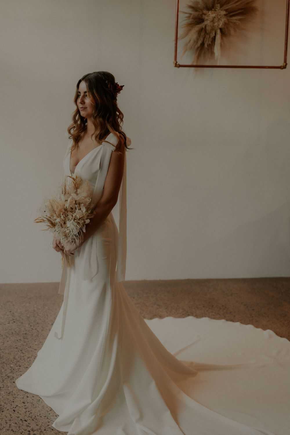 Elegant V-neck wedding gown with flowing train and dried flower bouquet.