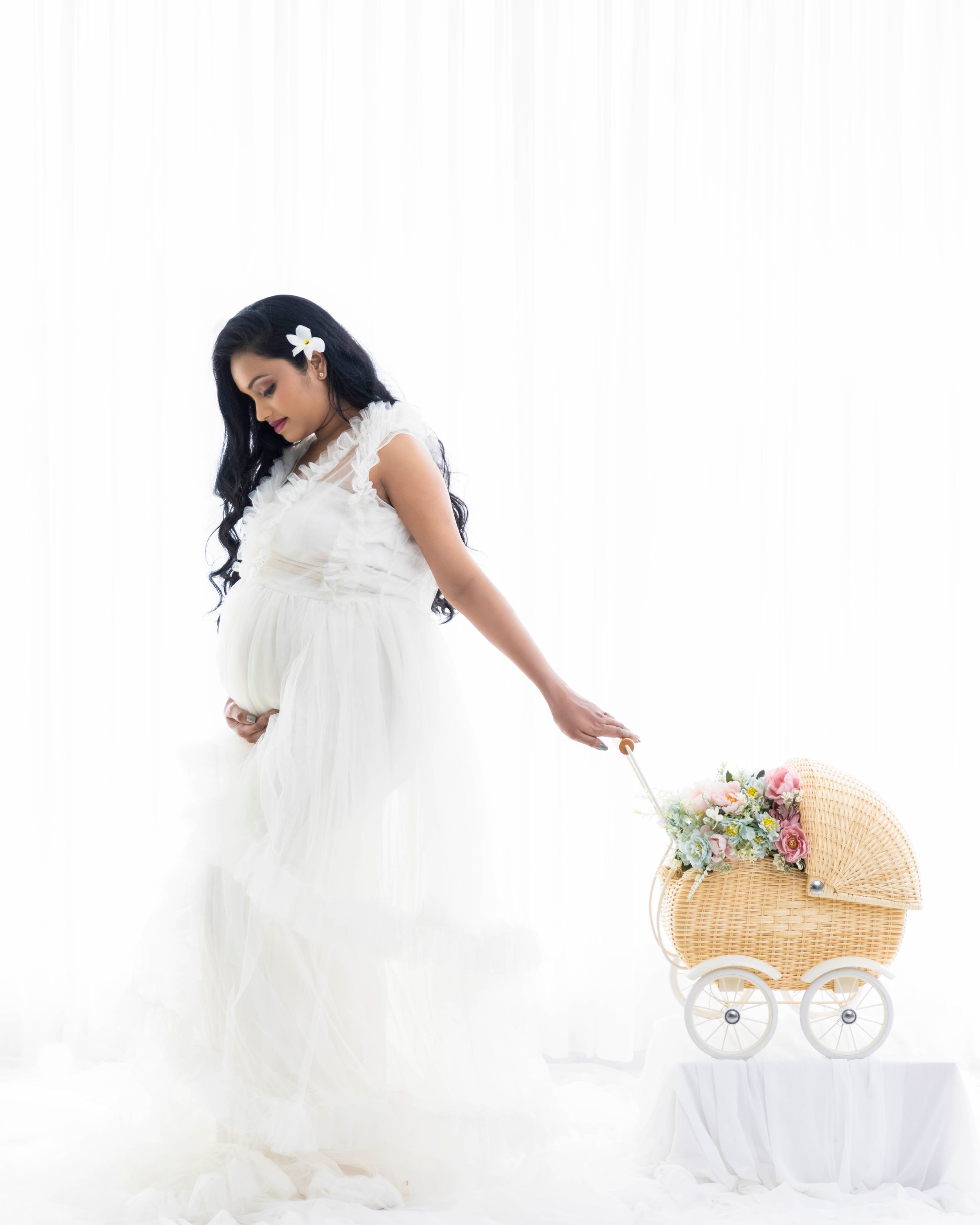 Maternity photo in white lace dress with vintage wicker baby carriage prop.