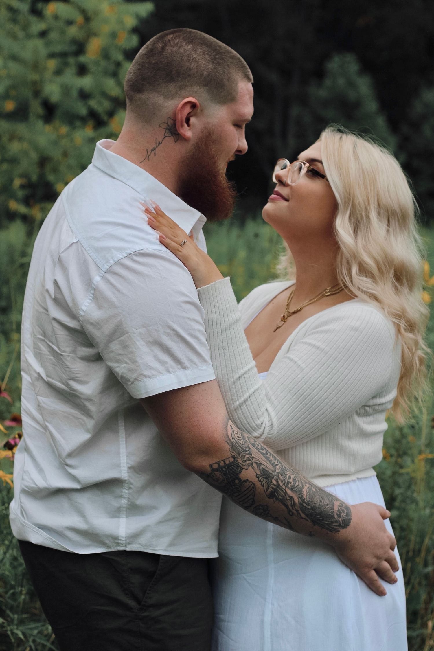 Romantic outdoor engagement portrait of couple embracing in white outfits.