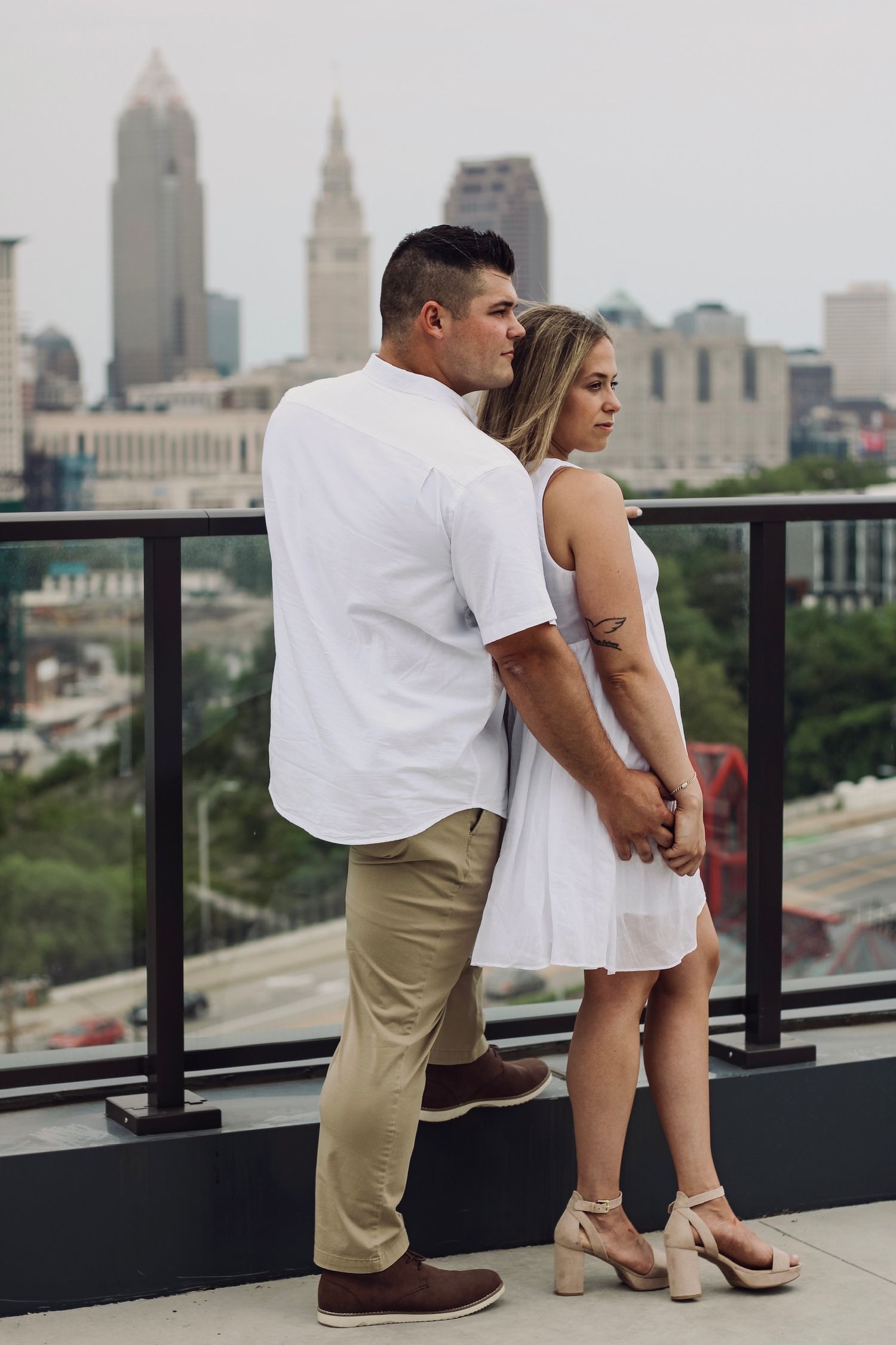 A couple embraces on a rooftop terrace with Cleveland's skyline in the background.