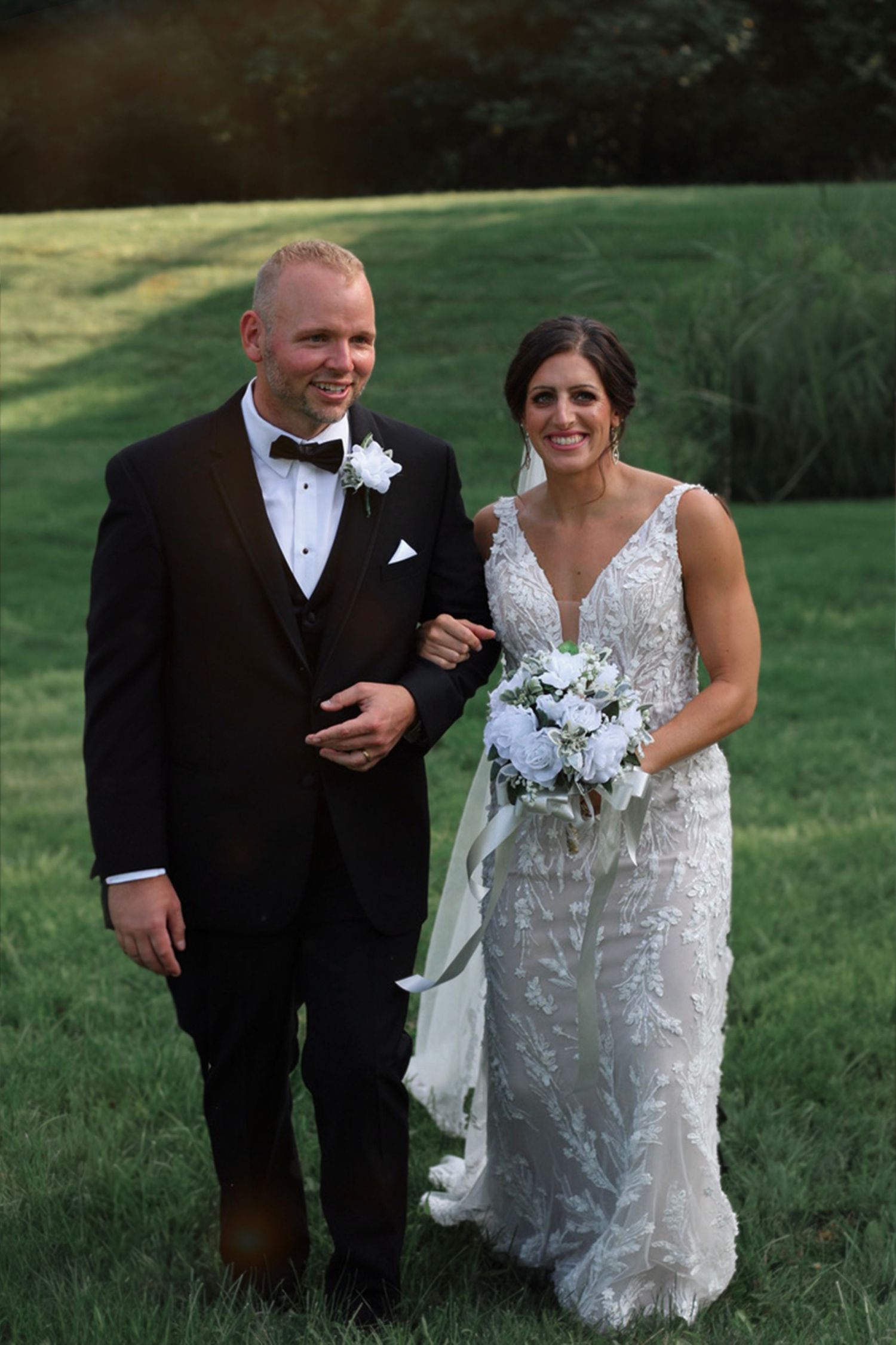 Wedding couple poses with bouquet on scenic grassy hillside.