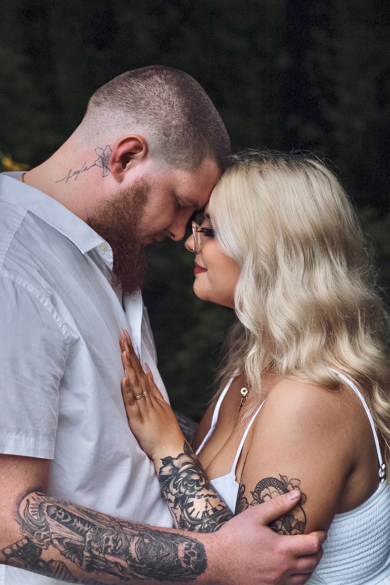 Intimate close-up of couple with tattoos sharing tender moment outdoors.