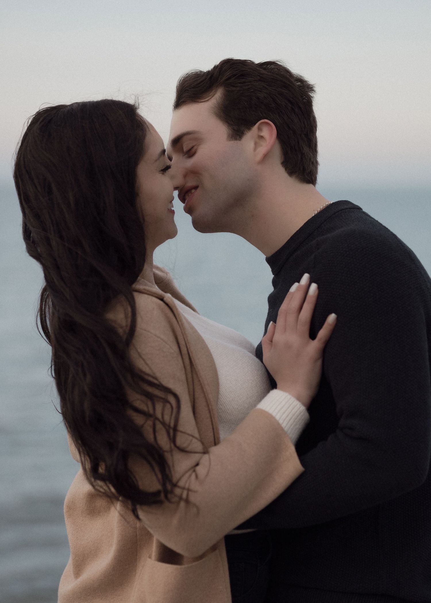 Intimate romantic moment between a couple embracing by the ocean during golden hour.