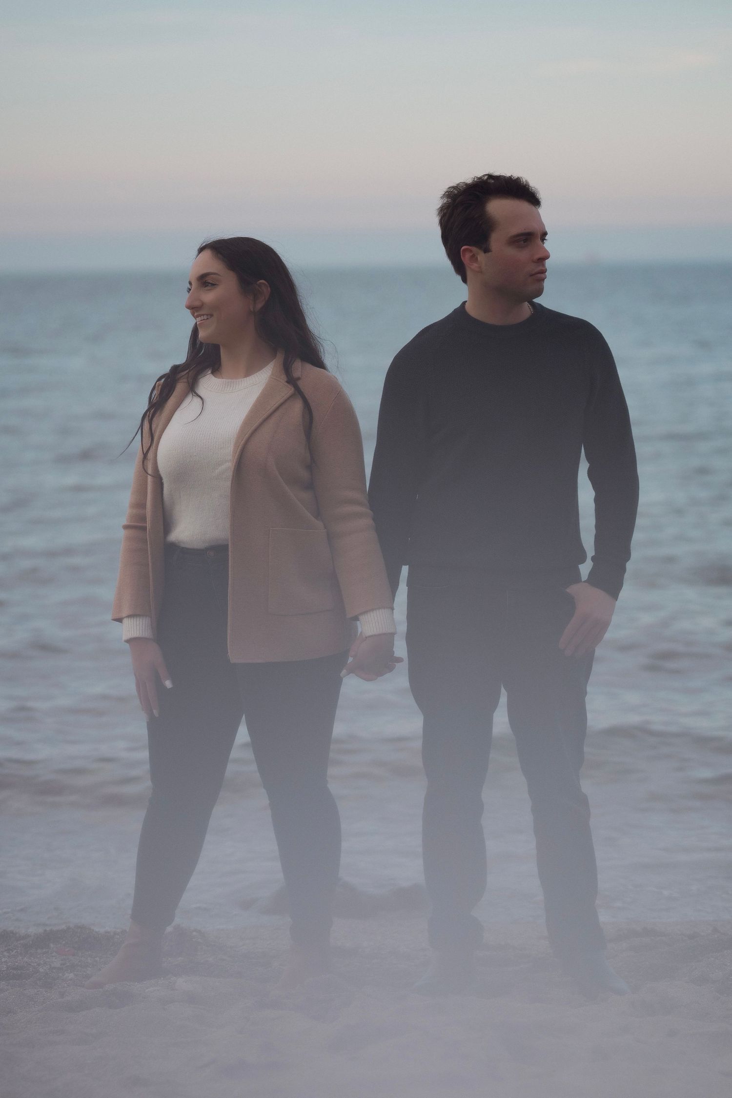 Couple standing together on a misty beach at dusk wearing coordinated casual outfits.