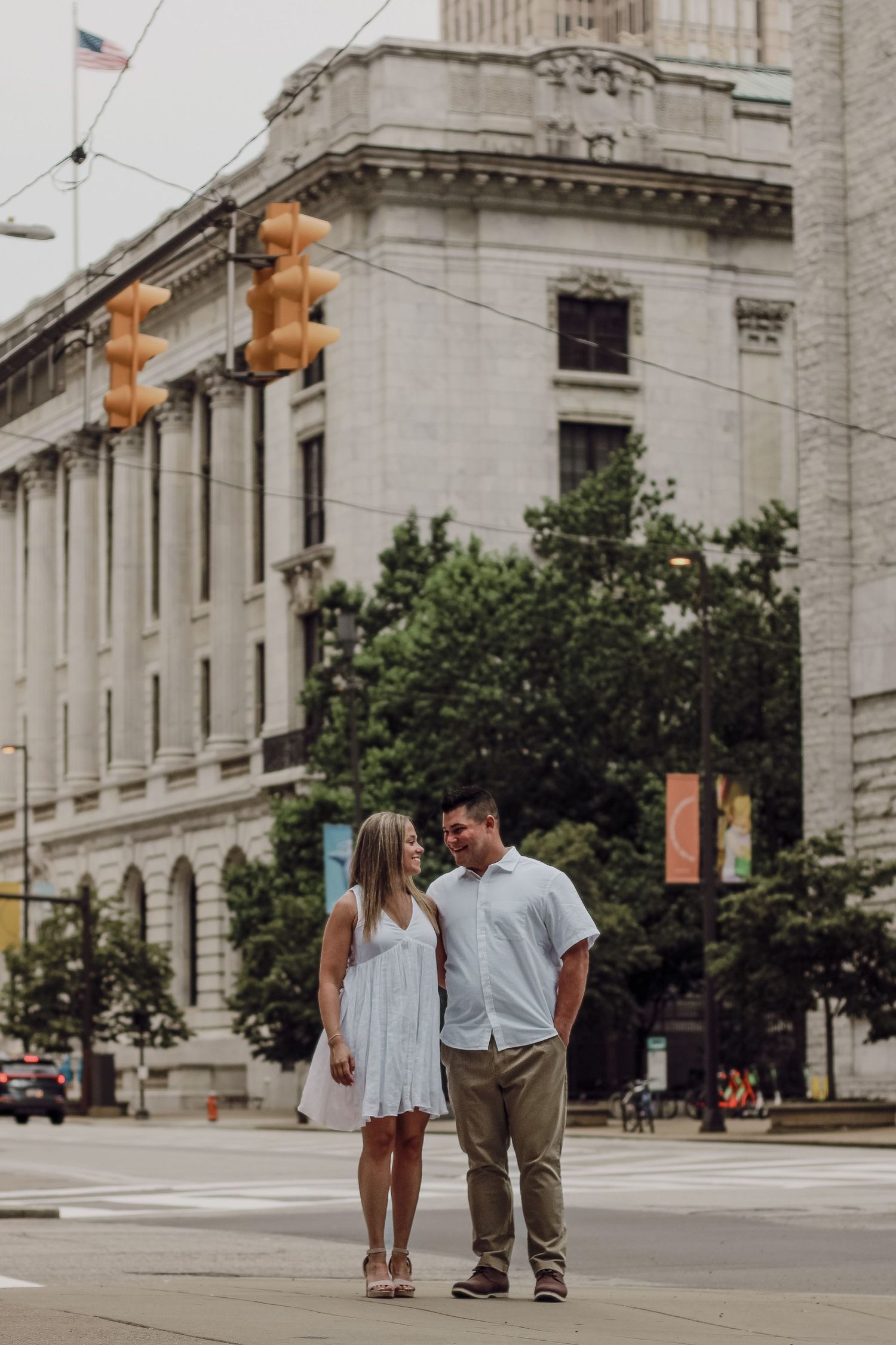 A couple strolls together in front of a historic building with traffic lights in an urban setting.