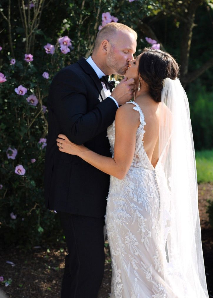 A romantic wedding moment captured against blooming purple flowers in a garden setting.
