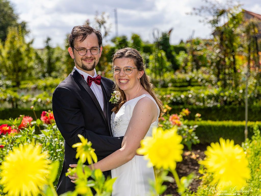A couple poses in a garden with vibrant yellow flowers blooming in the foreground.