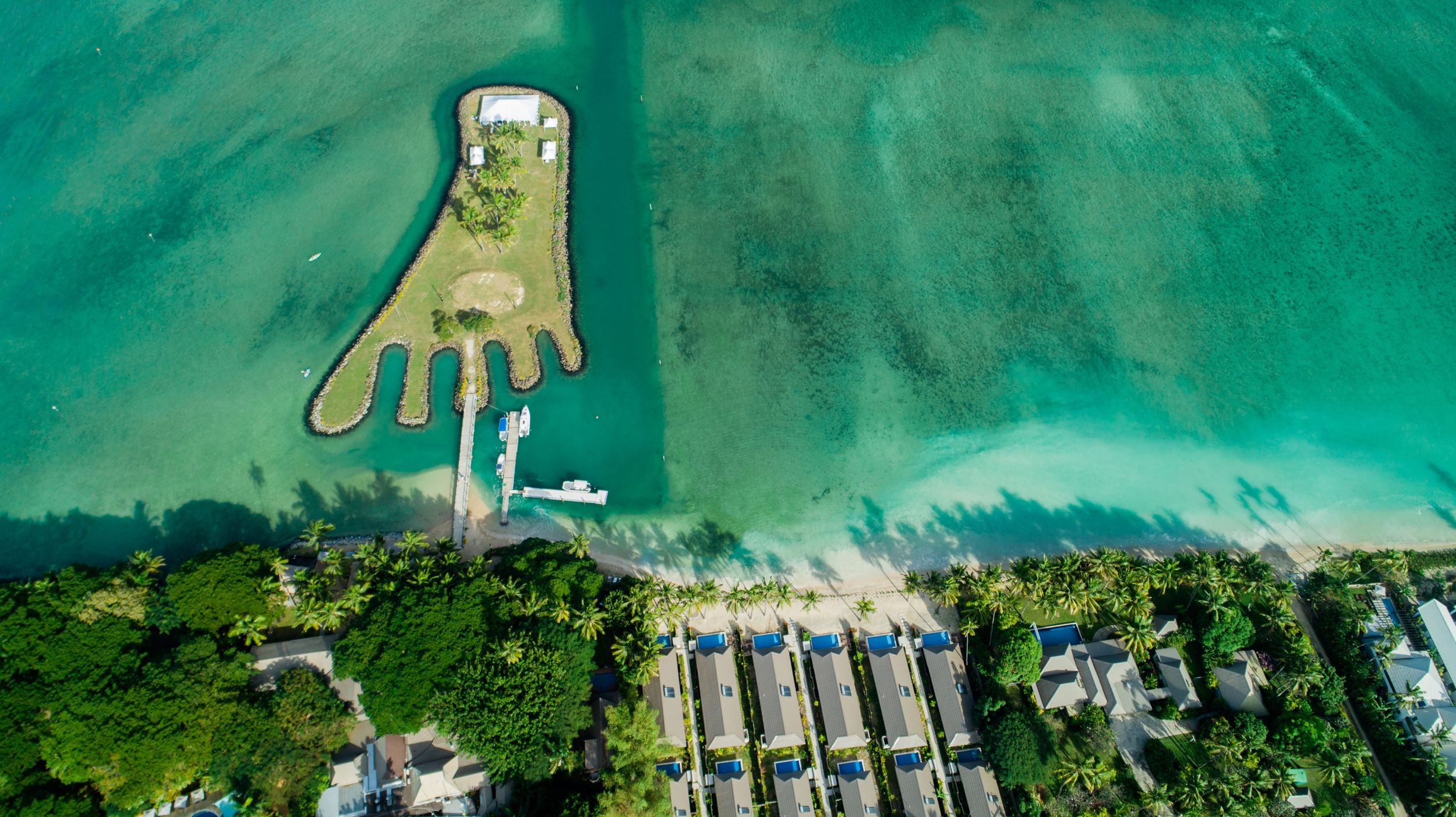 Aerial view of a beachfront resort property with docks and boats surrounded by turquoise waters.