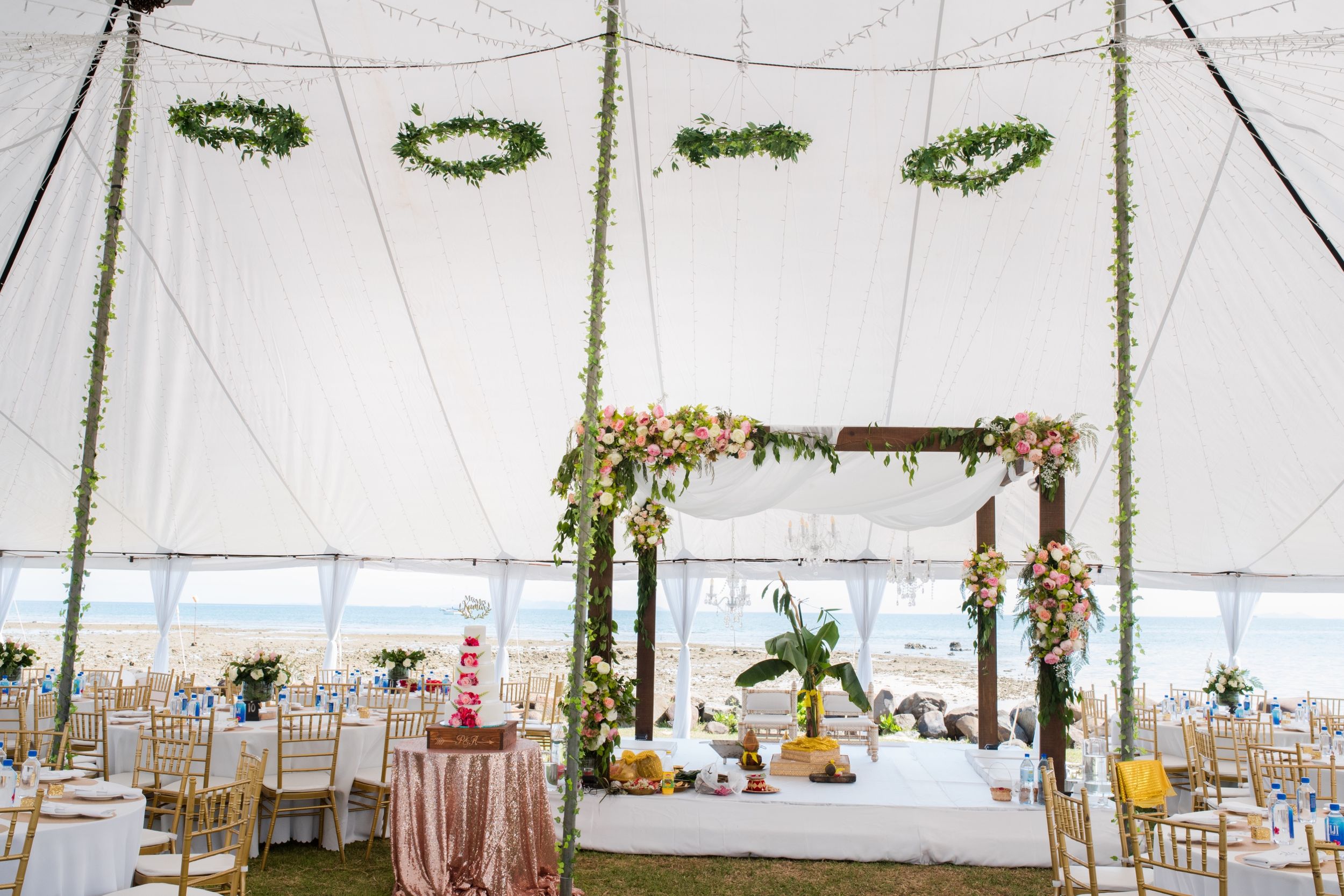 Elegantly decorated wedding tent interior with floral arrangements and hanging greenery wreaths.