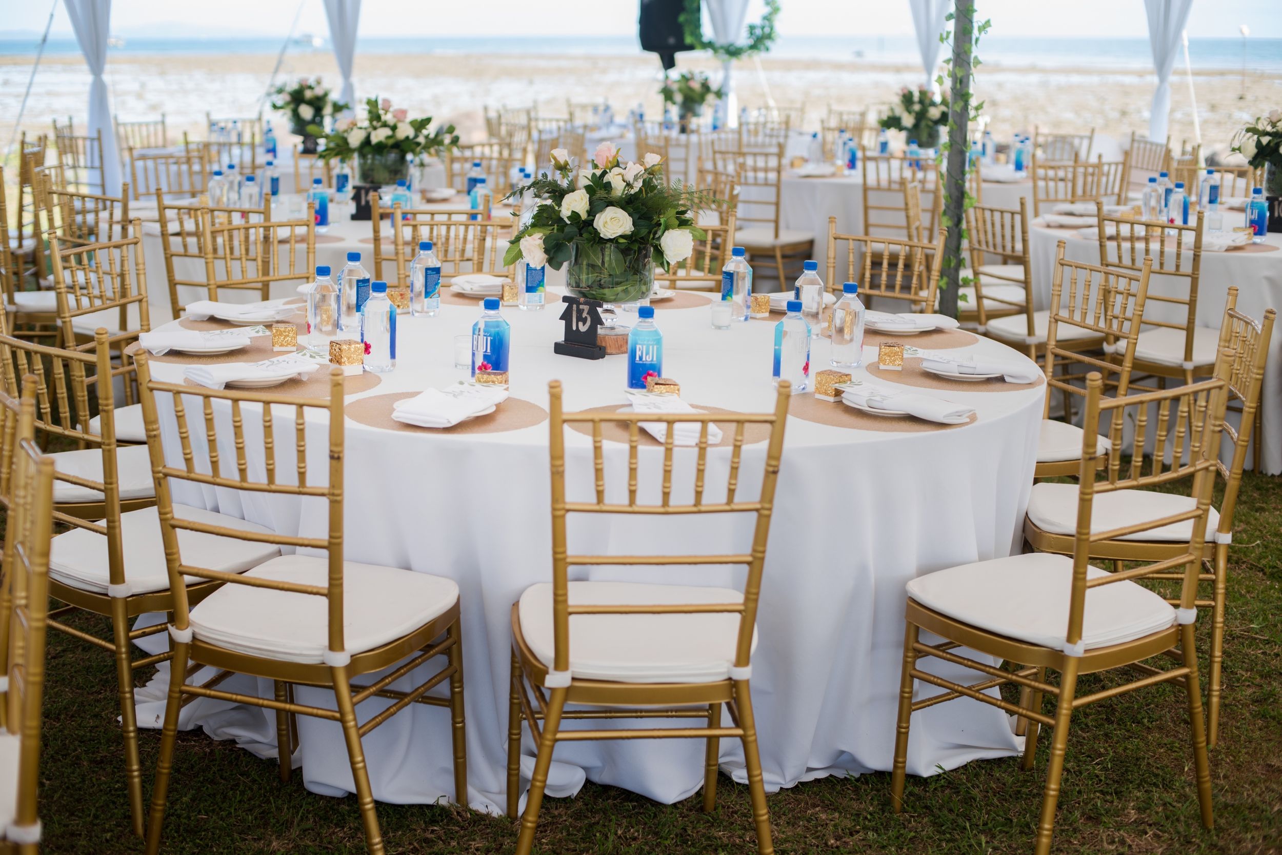 Elegant wedding reception setup with gold chiavari chairs and round tables under a white tent.