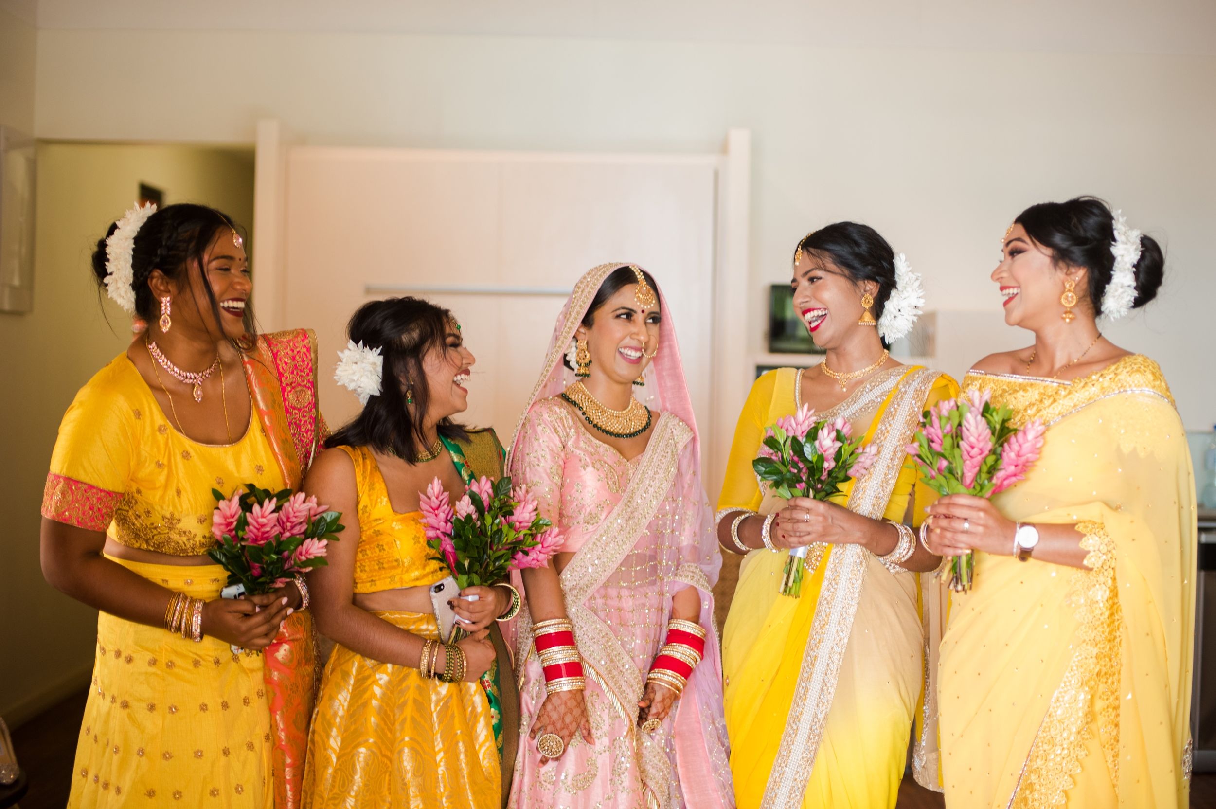 Wedding party in yellow and pink traditional Indian attire sharing joyful moments together.