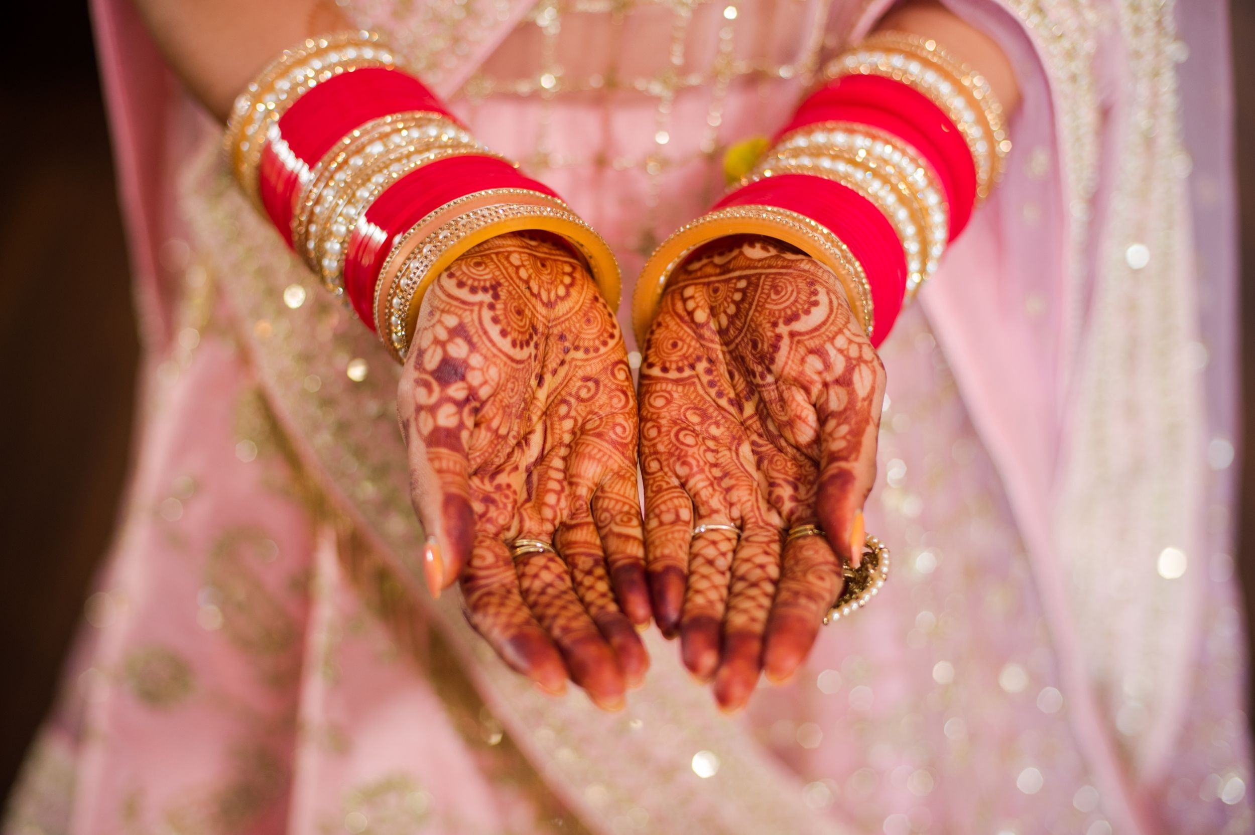 Detailed shot of intricate henna designs on hands with red wedding bangles and sparkly fabric.