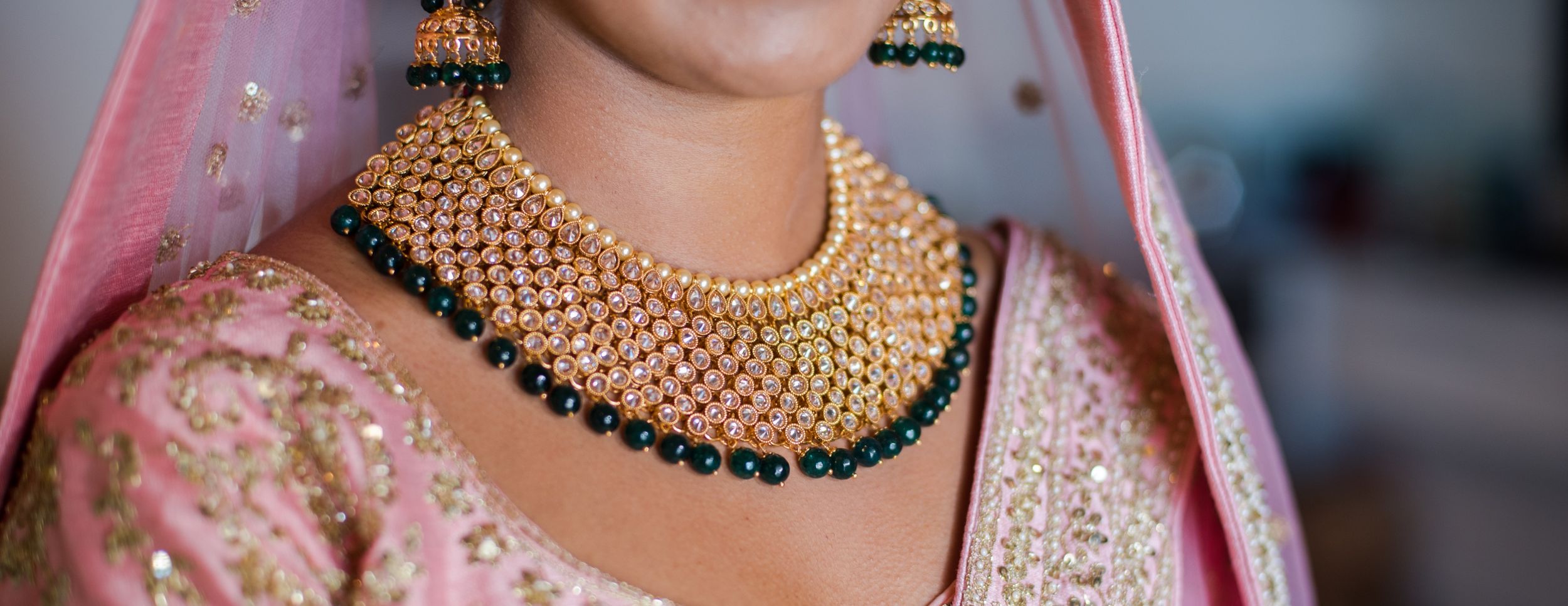Close-up of ornate gold and emerald wedding necklace with pink traditional bridal outfit.