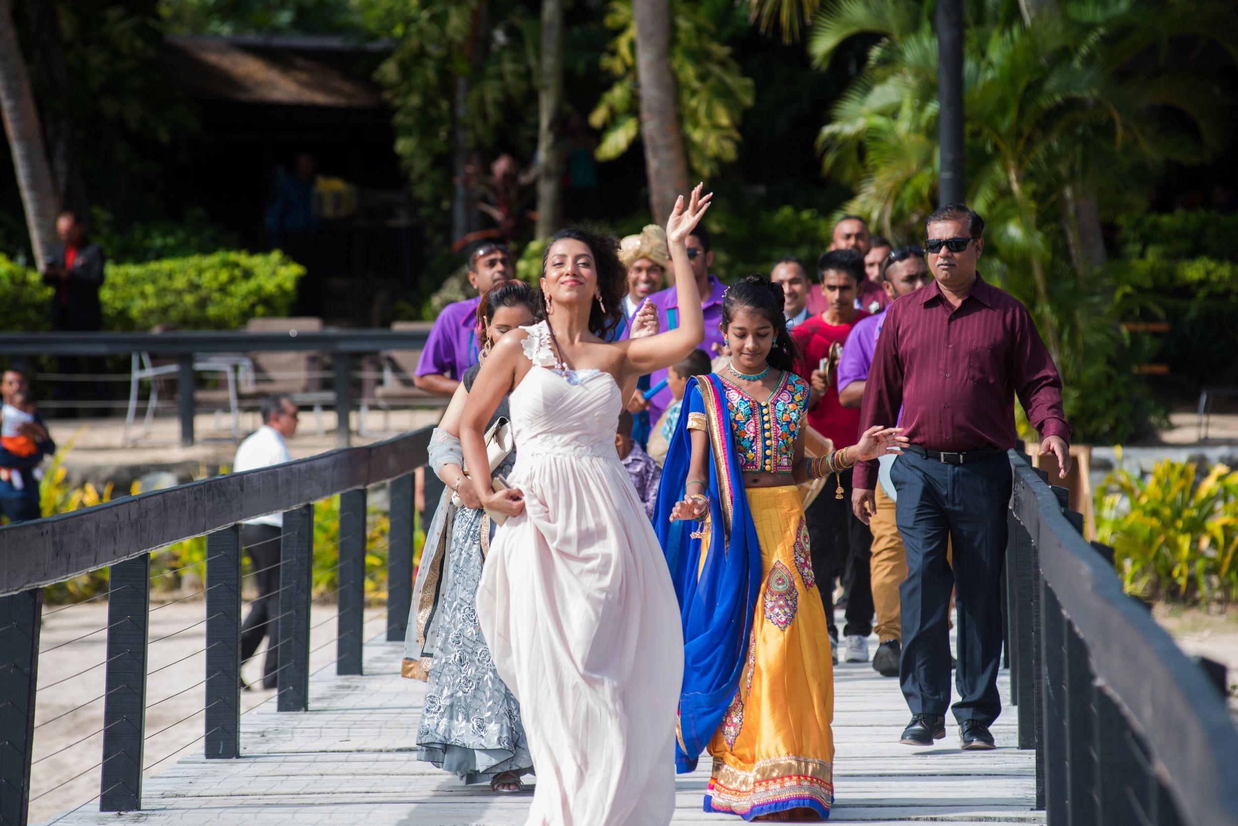 Wedding procession walking along tropical resort pathway with colorful traditional attire.