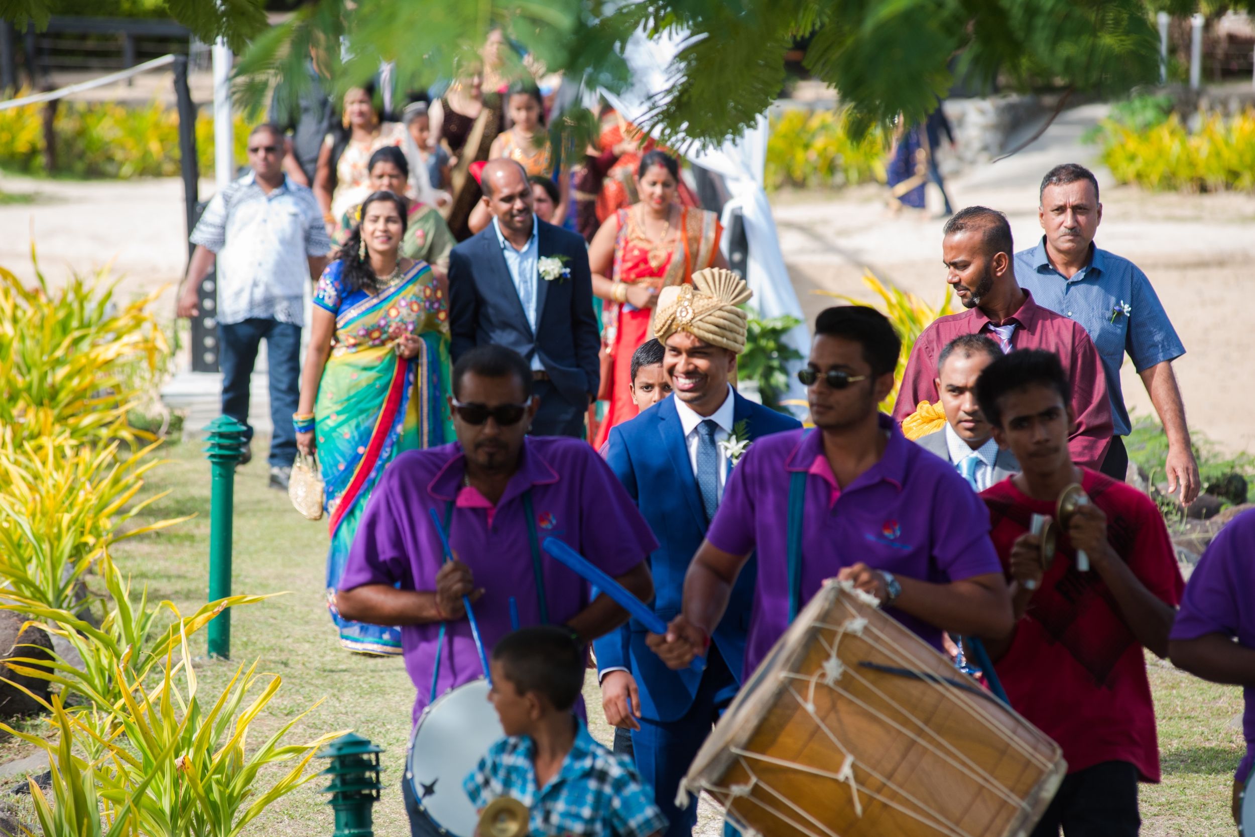 Festive wedding procession with traditional drummers and guests in vibrant attire.