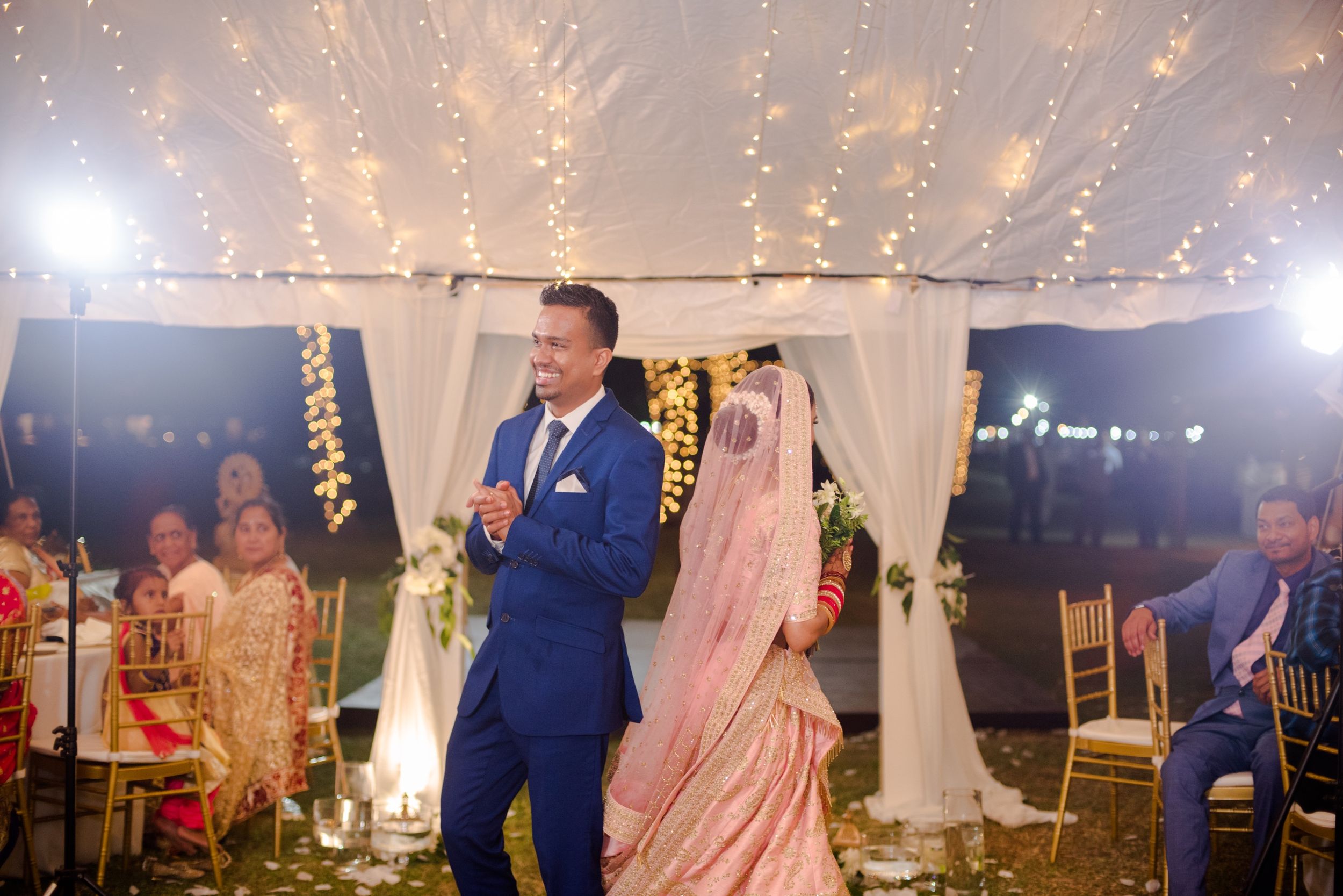 Evening wedding reception under tent with sparkling lights and elegant white draping.