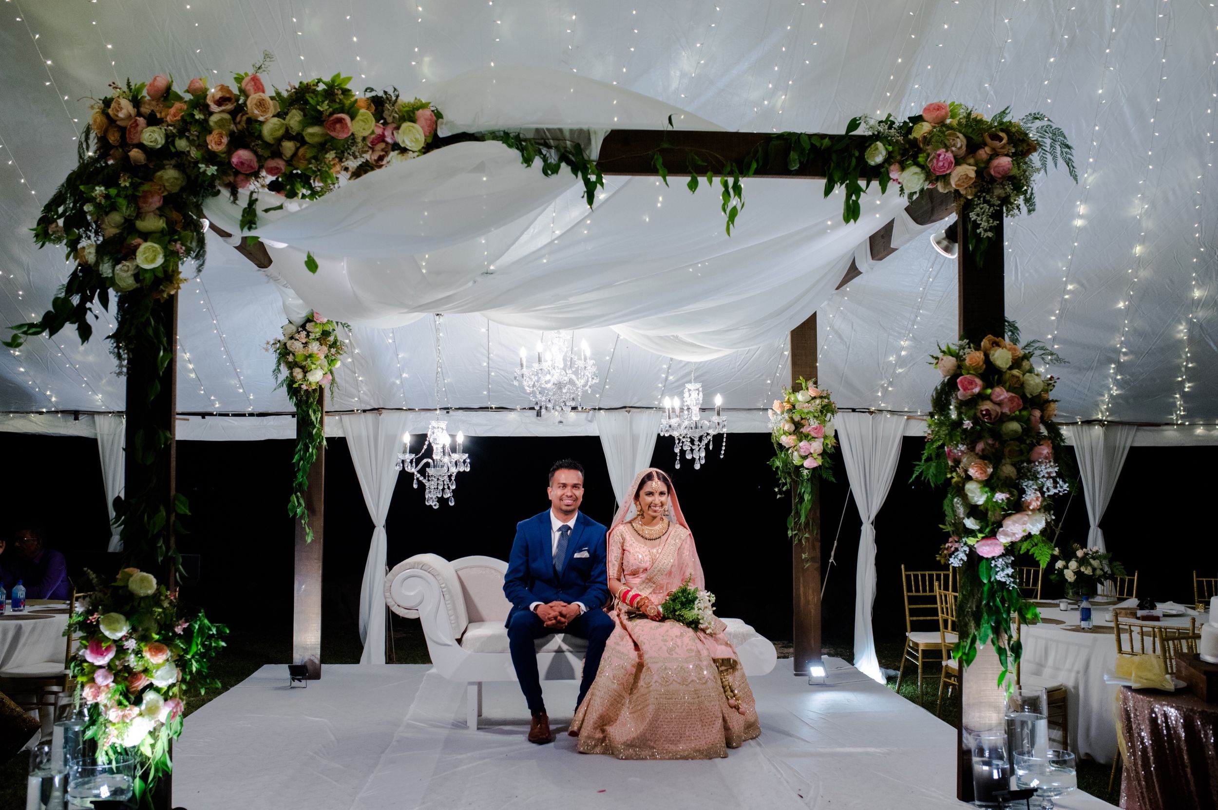 Elegant wedding setup with floral arch and white decor under a tent with string lights.