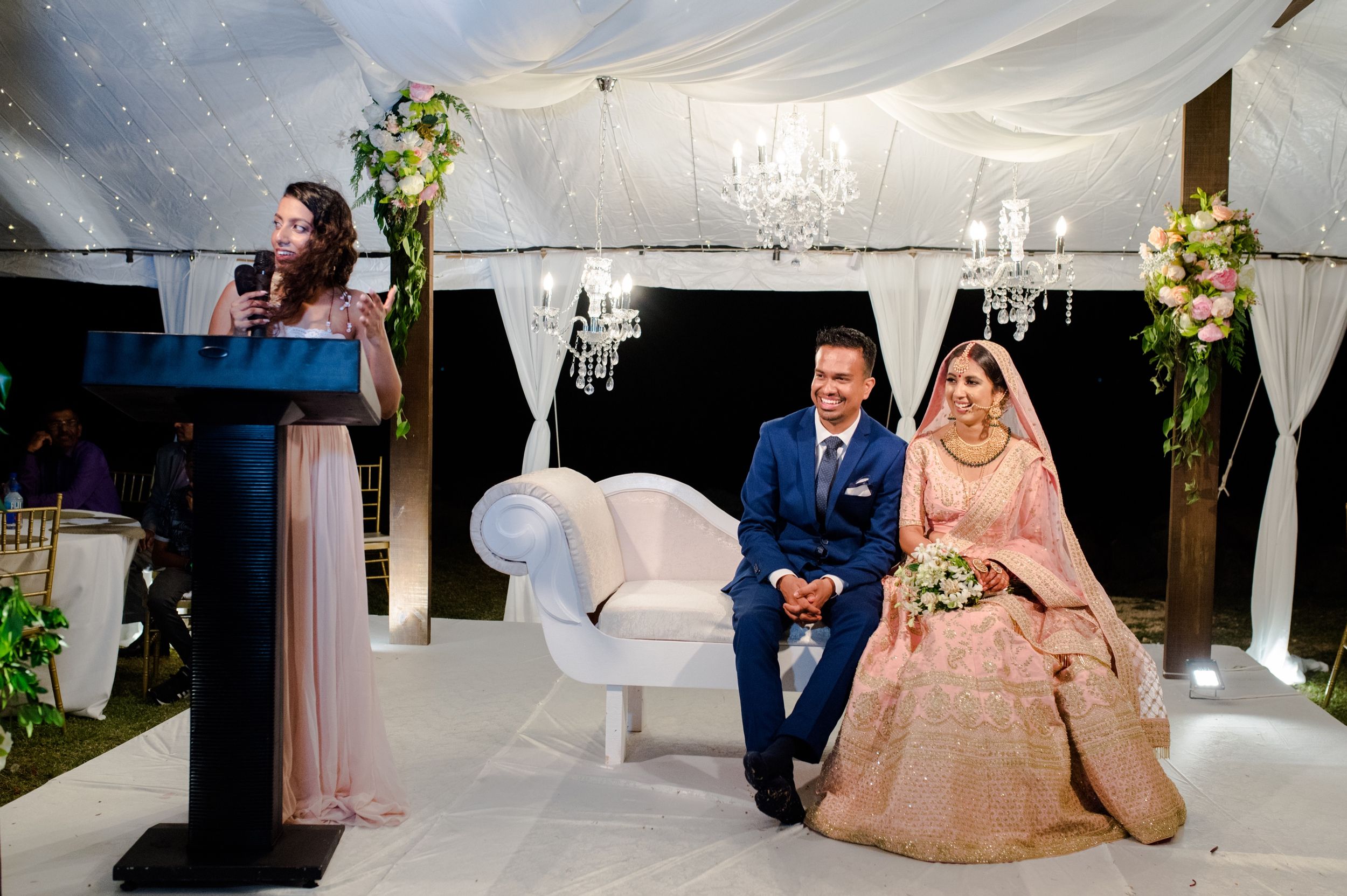 Wedding ceremony setup with elegant white decor, chandeliers and floral arrangements.