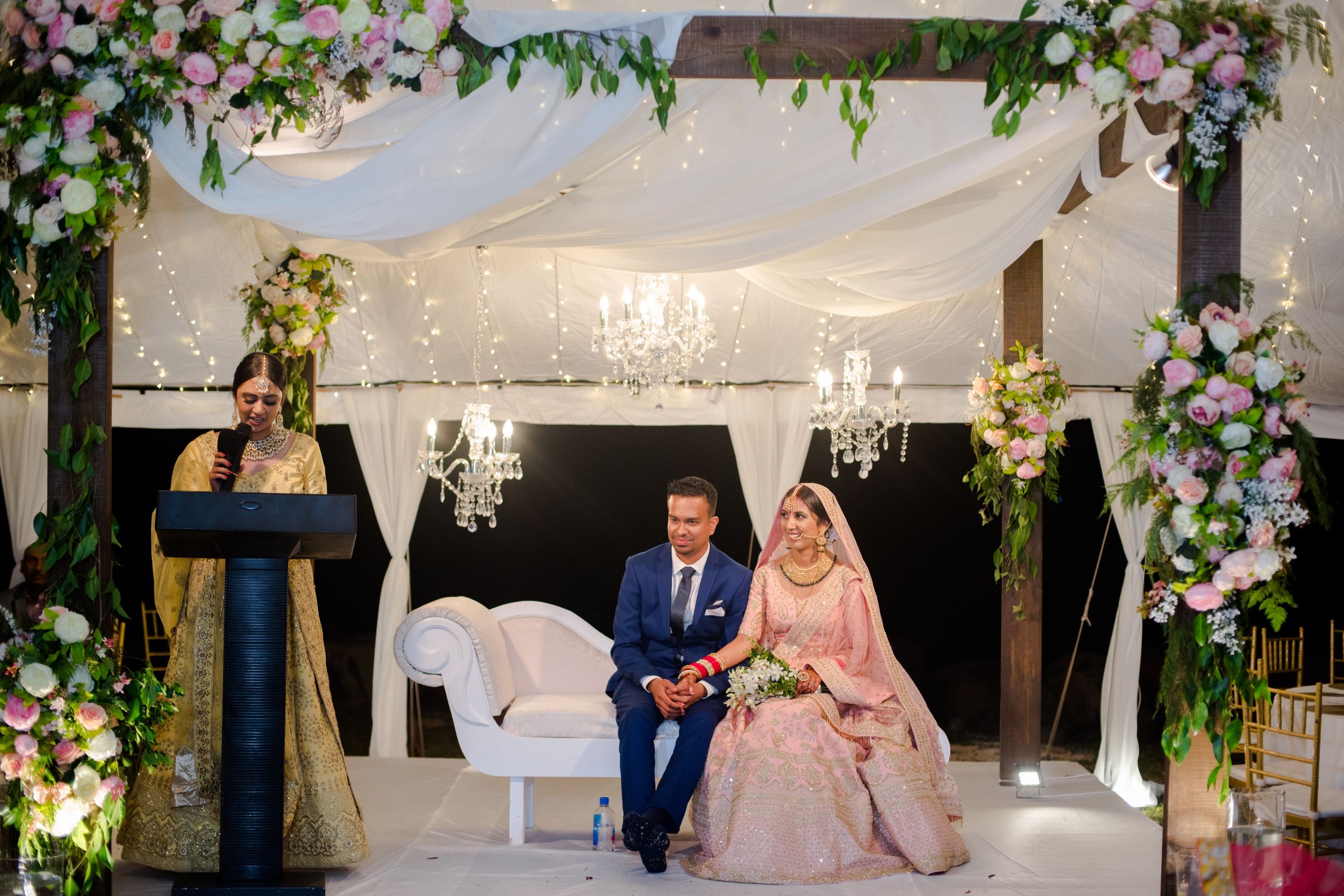 Decorated wedding venue with white draping, crystal chandeliers and pink floral arrangements.
