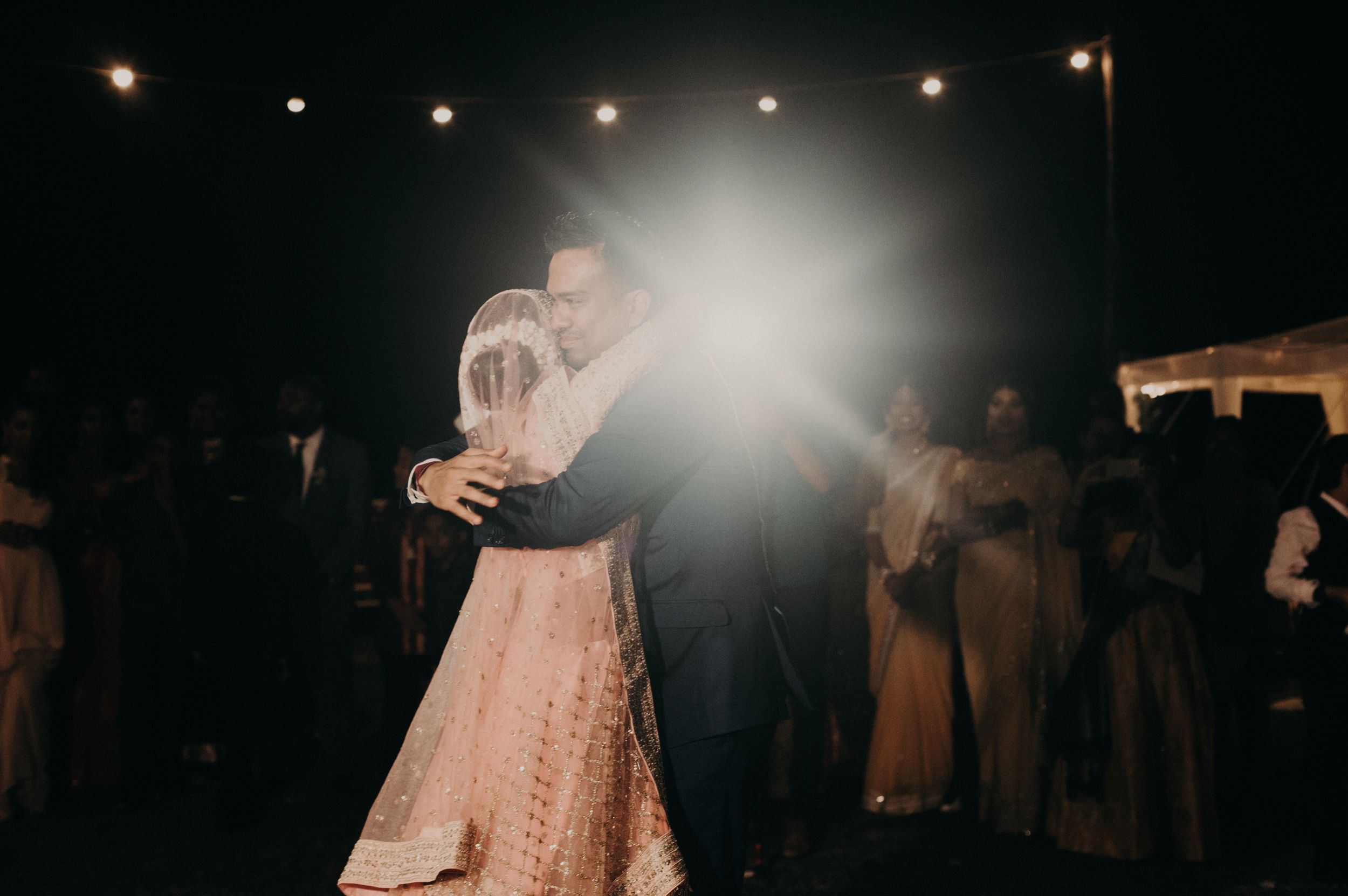 A romantic dance moment captured with dramatic backlighting at an evening wedding celebration.