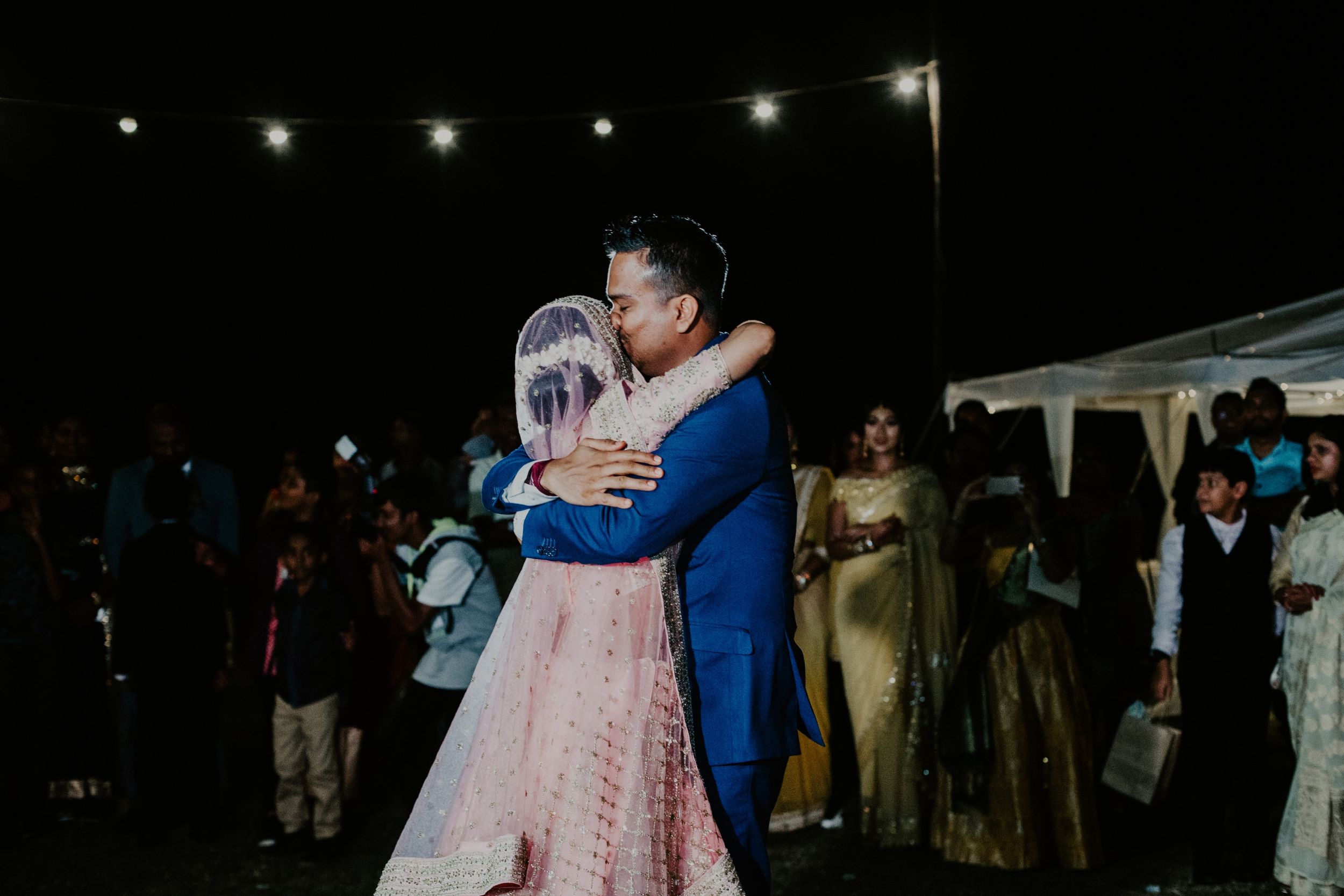 A couple sharing a dance under string lights at their outdoor wedding reception.