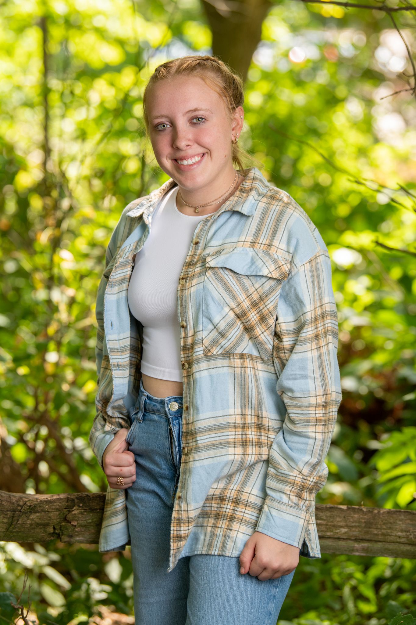 Casual outdoor portrait in a plaid flannel shirt and jeans against lush green foliage.