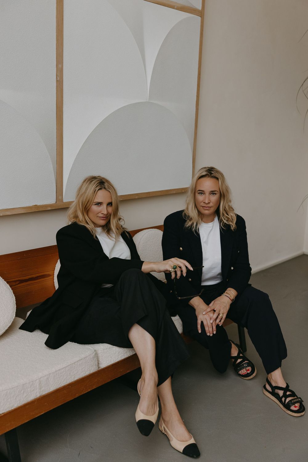 Two people in matching black and white outfits seated on wooden bench with geometric wall art.
