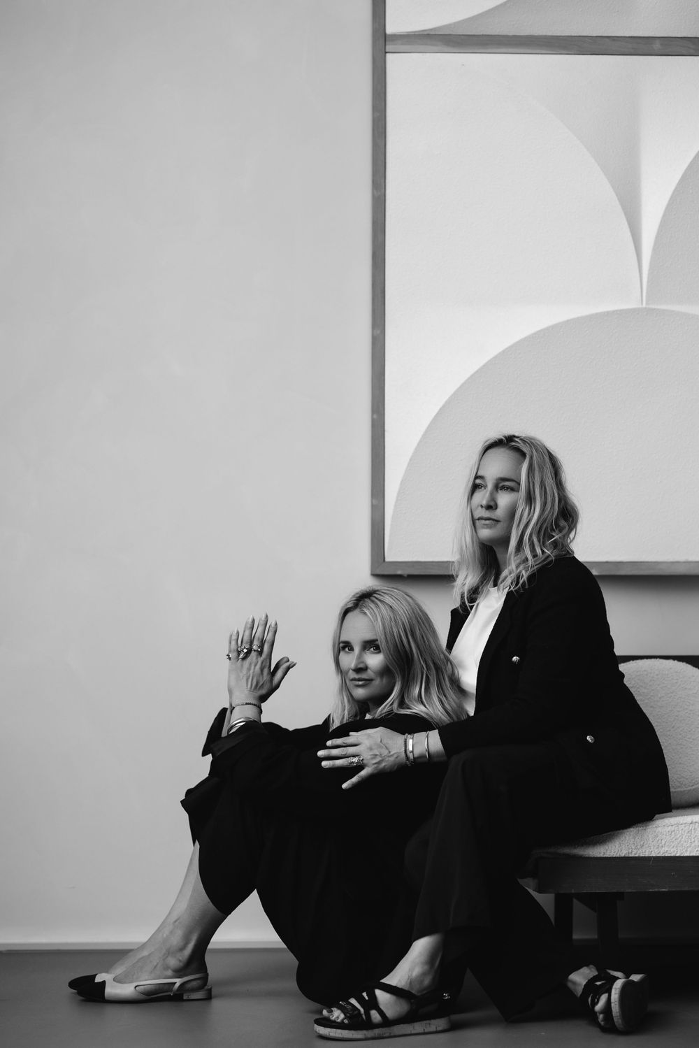 Artistic black and white portrait of two women sitting against minimalist wall decor.