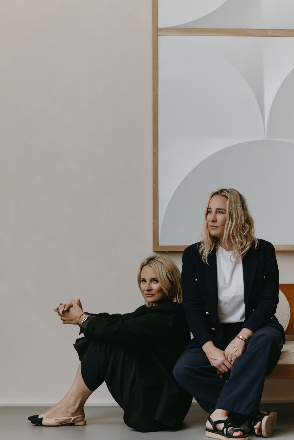 Two women in black and white outfits posing against geometric wall art.