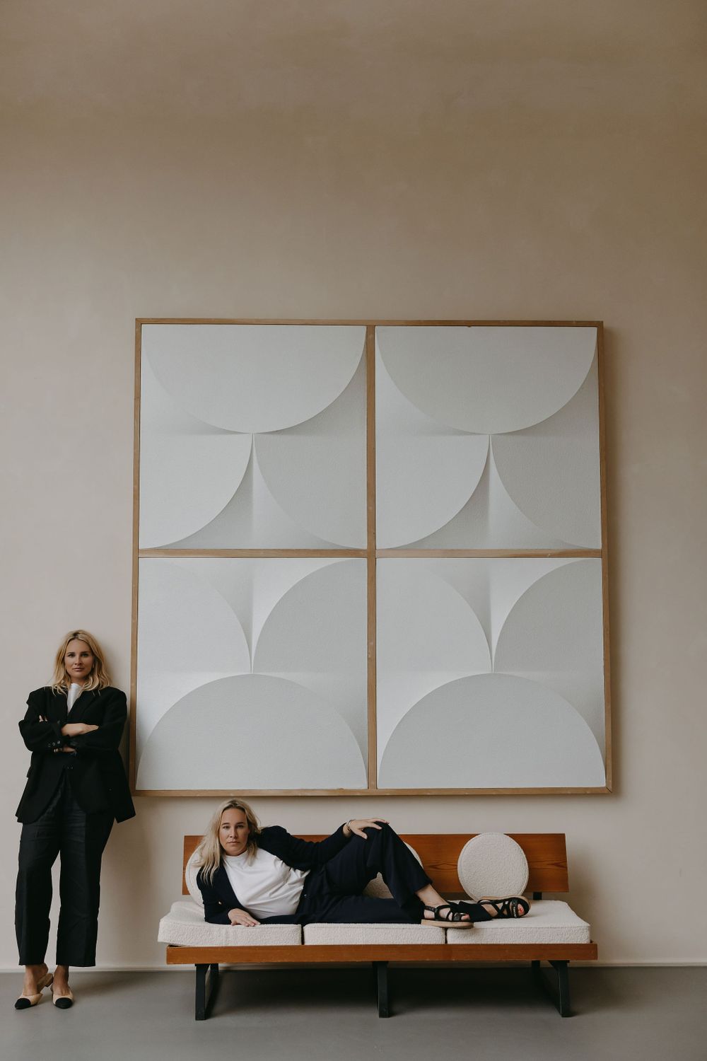 Modern minimalist photo with geometric wall art and two women on bench.