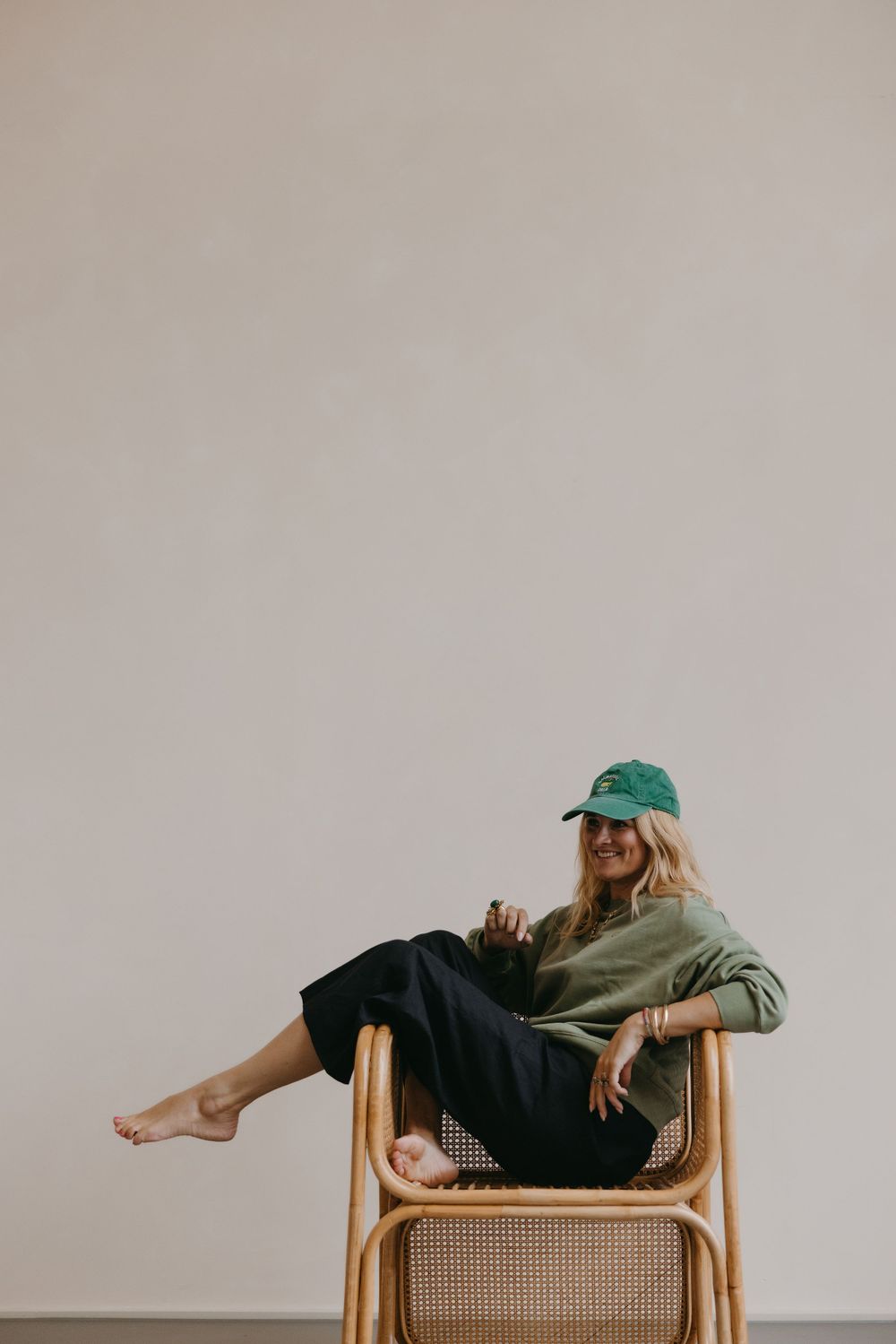 Woman relaxing in casual attire and green cap on wicker chair.