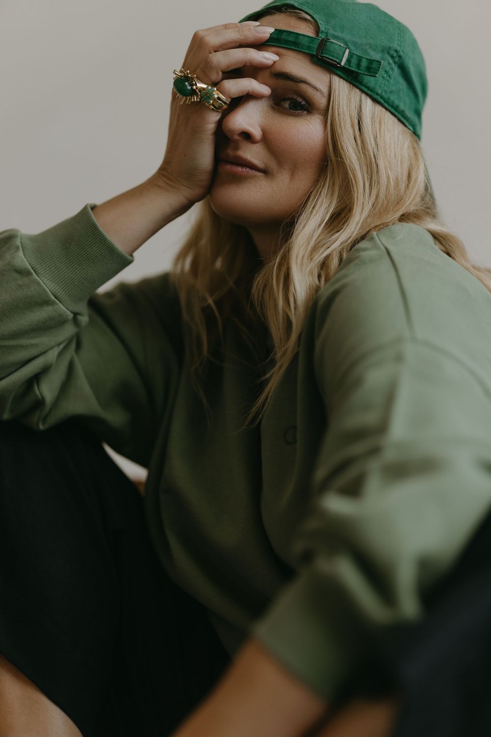 A moody fashion portrait featuring olive green sportswear and a matching baseball cap accessorized with rings.