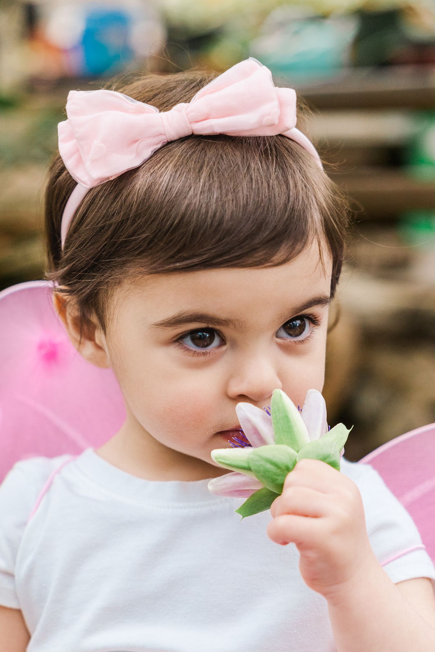 A figure wearing a pink bow holds up a flower bud in a garden scene.