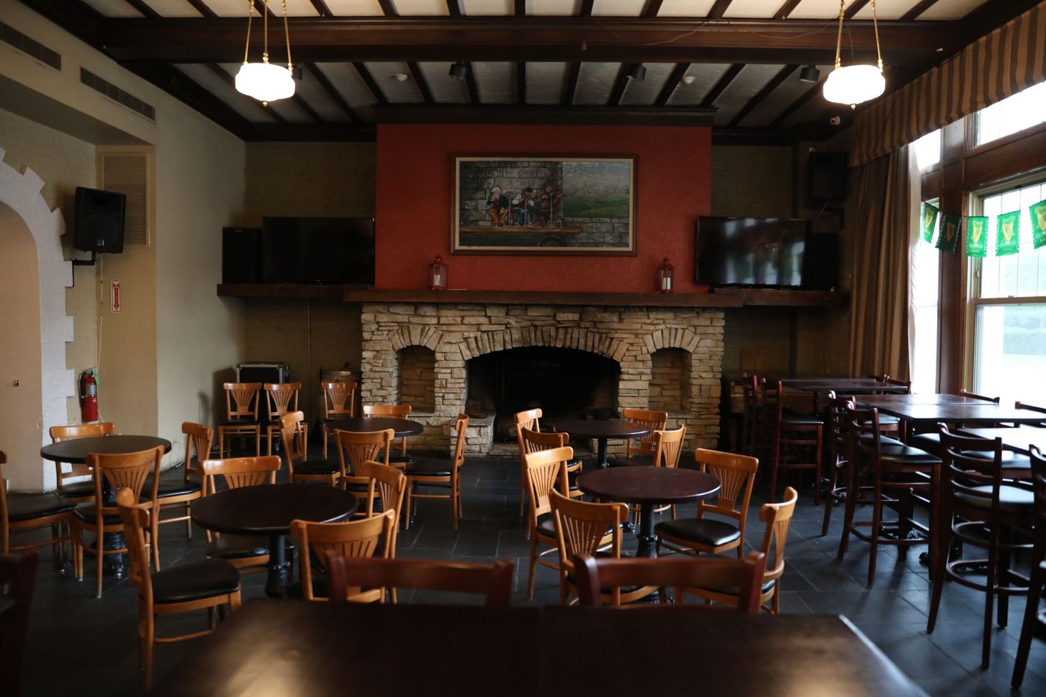 Rustic restaurant interior with stone fireplace, wooden beams, and scattered tables and chairs.